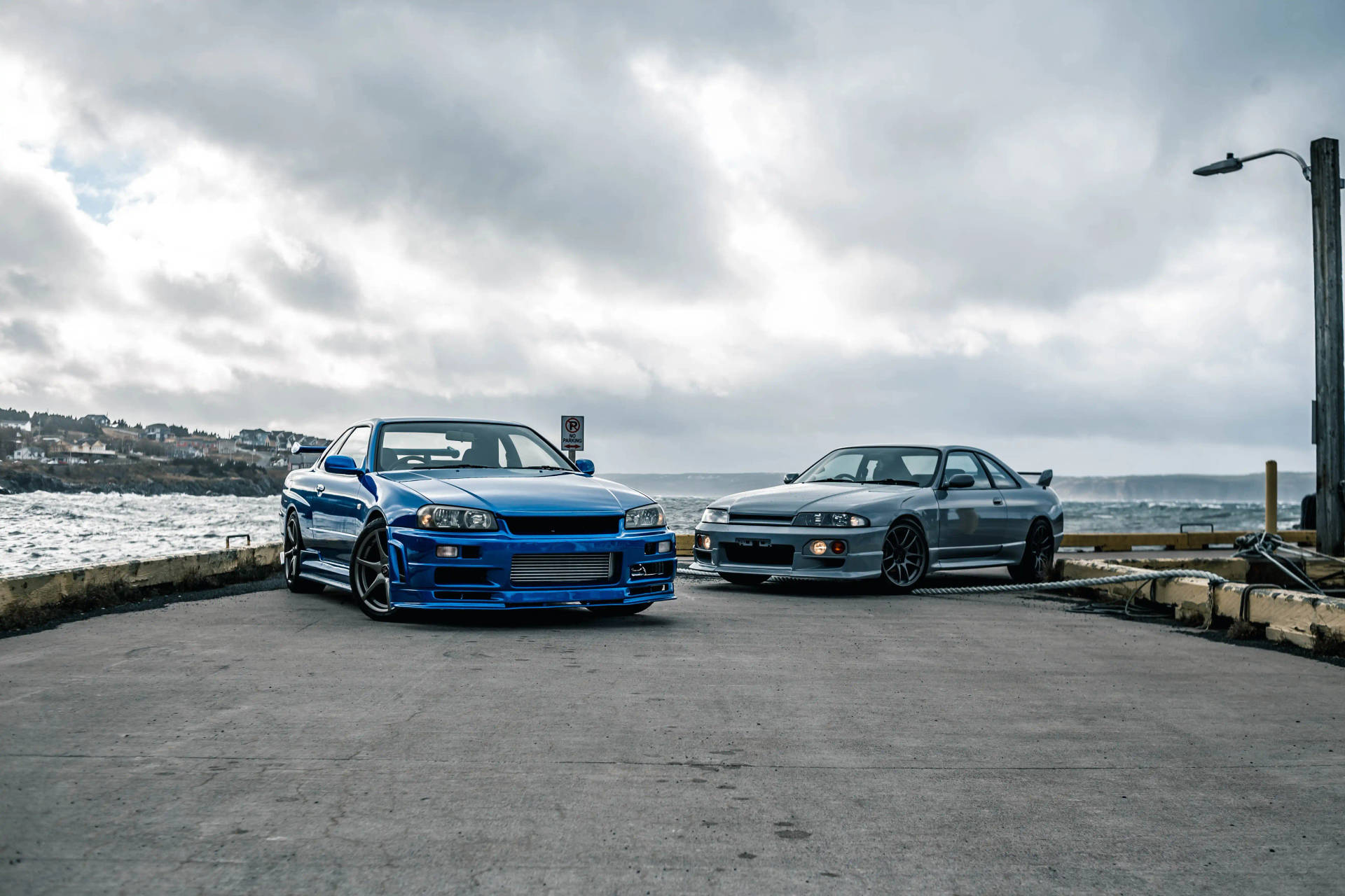 兩輛藍色和銀色的日產Skyline GT-R停泊在海邊碼頭上。