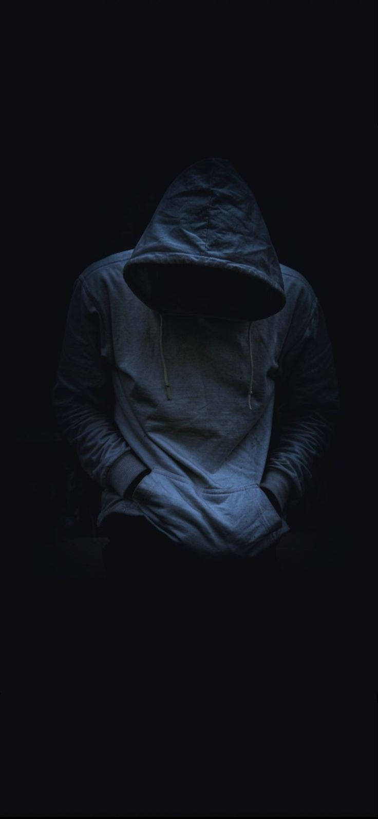 一個穿連帽衫的人在黑暗中低著頭，雙手插袋。