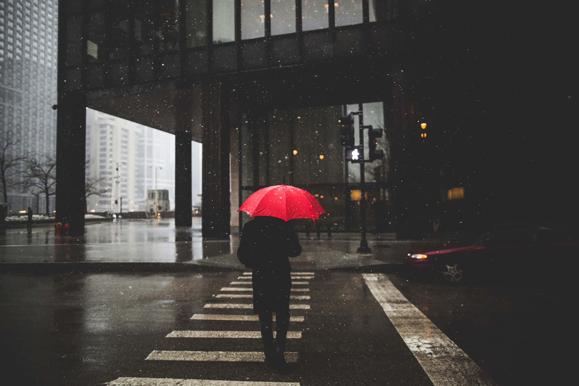 壁紙 — 一個孤獨的身影撐著鮮紅色雨傘，在夜間雨中走過濕漉漉的城市街道。