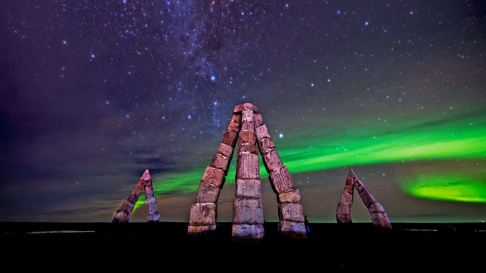 發光綠色北極光和星空下的石柱