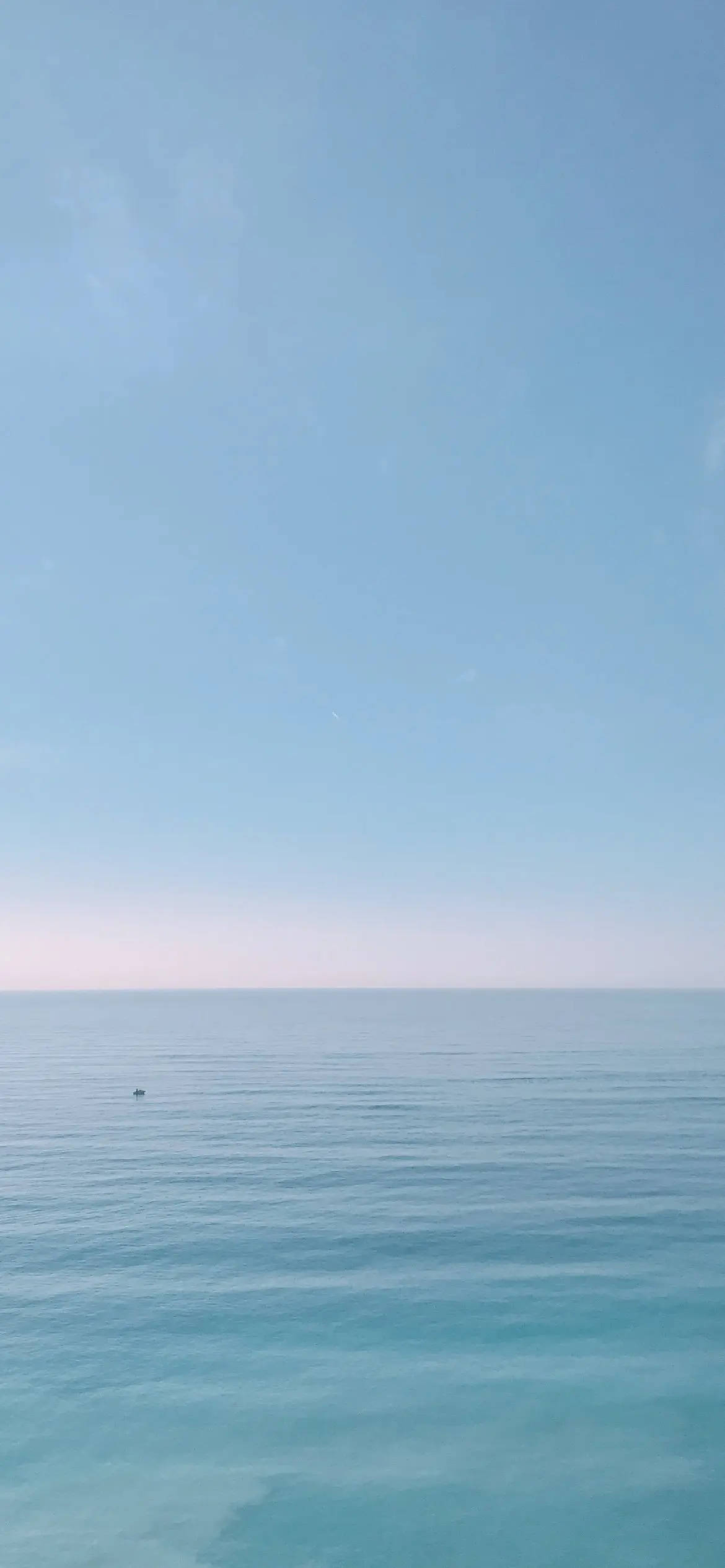 晴朗天空下平靜的碧綠海洋，地平線上有小船