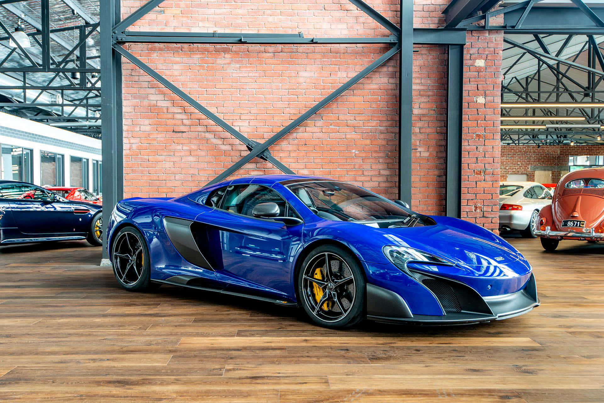 Mclaren 675lt Spider 桌布 壁紙 — 一輛光亮的藍色McLaren跑車在明亮的燈光下，在帶有木地板的質樸磚鋼車庫中閃耀。