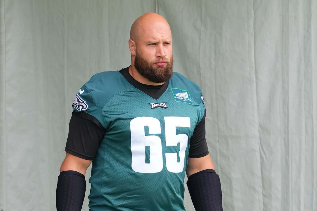  壁紙 — 一位光頭鬍鬚美式足球員身穿綠色Eagles球衣（65號），站在純灰色背景前。