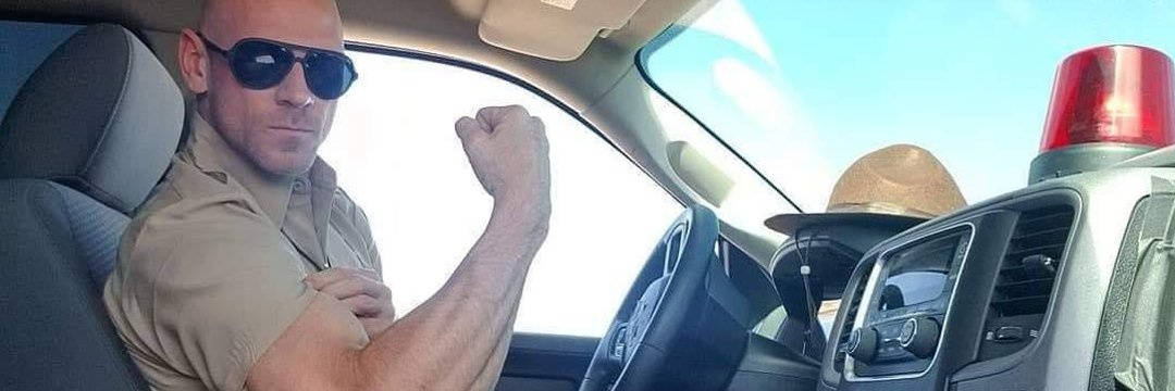 警員在車頂有紅燈的巡邏車內彎曲二頭肌。