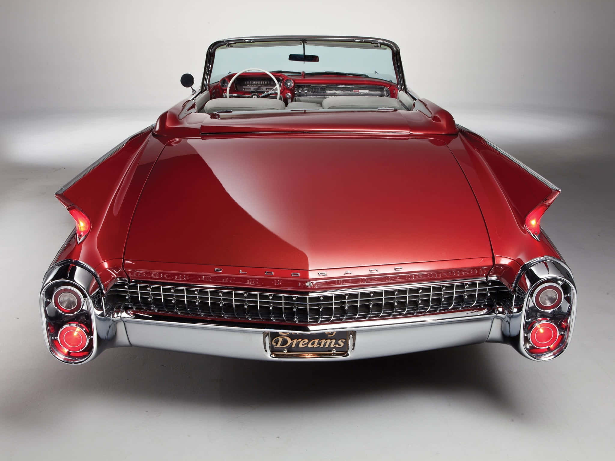 Cadillac Eldorado 桌布 壁紙 — 一輛光澤的紅色經典敞篷車，帶有鍍鉻裝飾和 'Dreams' 車牌，從正面展示在中性工作室背景前。