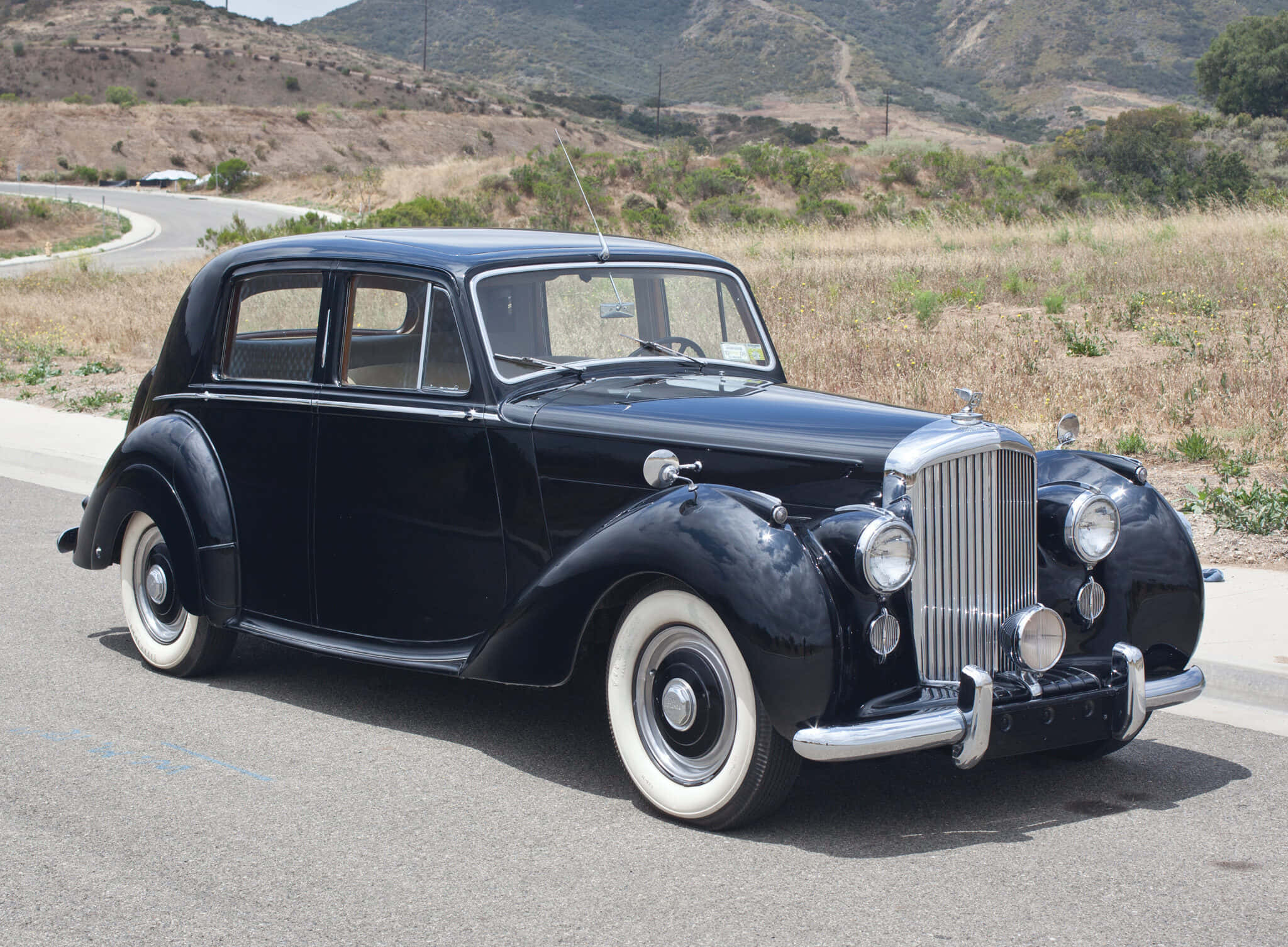 Bentley Mark Vi 桌布 壁紙 — 一輛光澤黑色復古轎車，配備白色側壁輪胎，在明亮的日光下停放在路邊。
