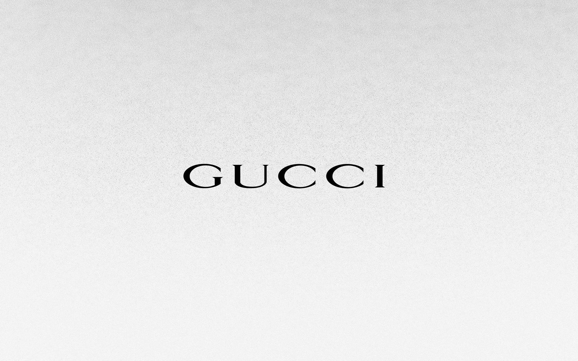 Gucci 桌布 壁紙 — Gucci 標誌以優雅的黑色襯線字體居中顯示在帶有紋理的淺灰色背景上。