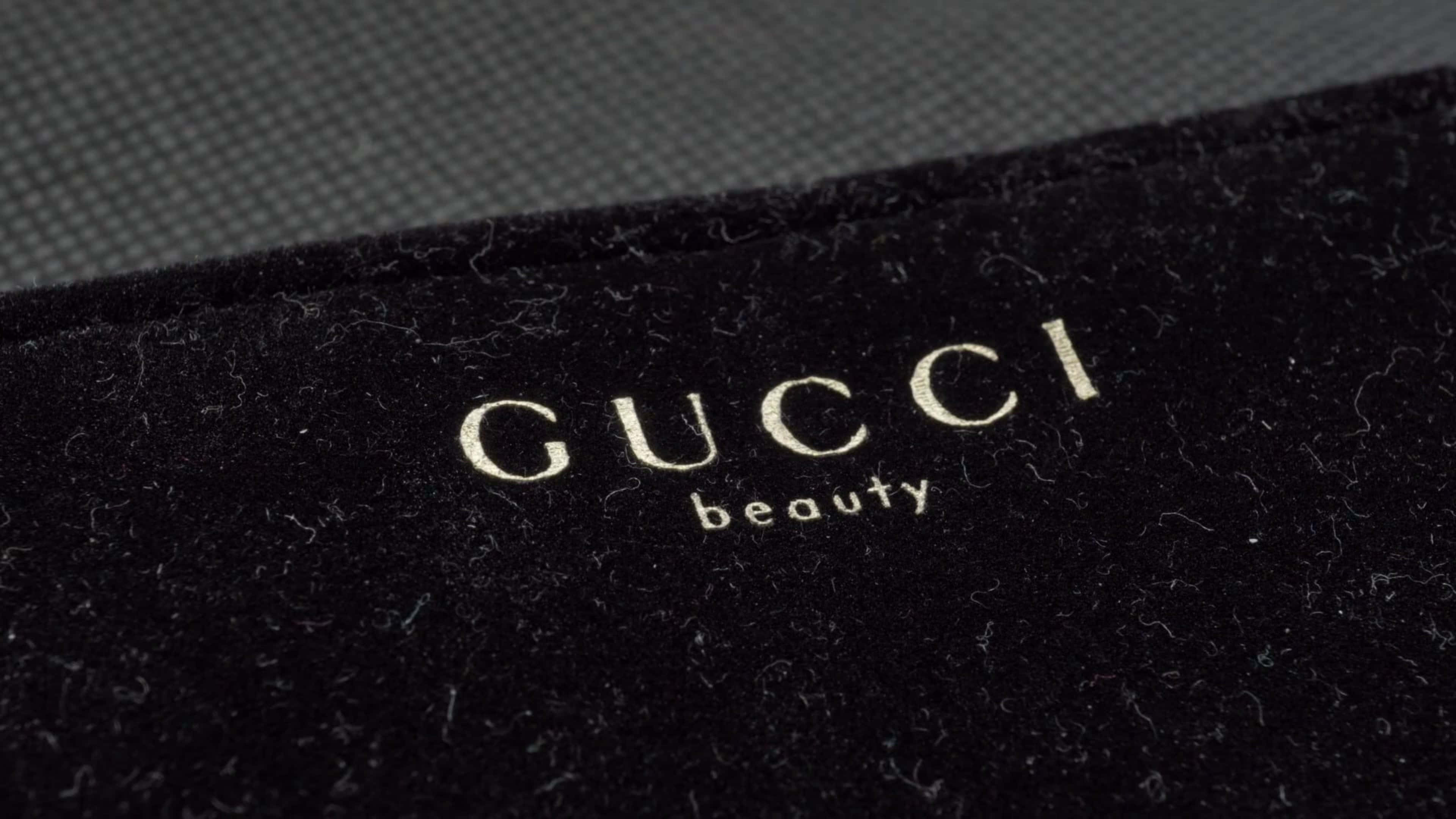 Gucci美妝特寫4K 壁紙 — 金色Gucci beauty標誌近距離特寫，繡在豪華黑色天鵝絨上，背景為紋理灰色。