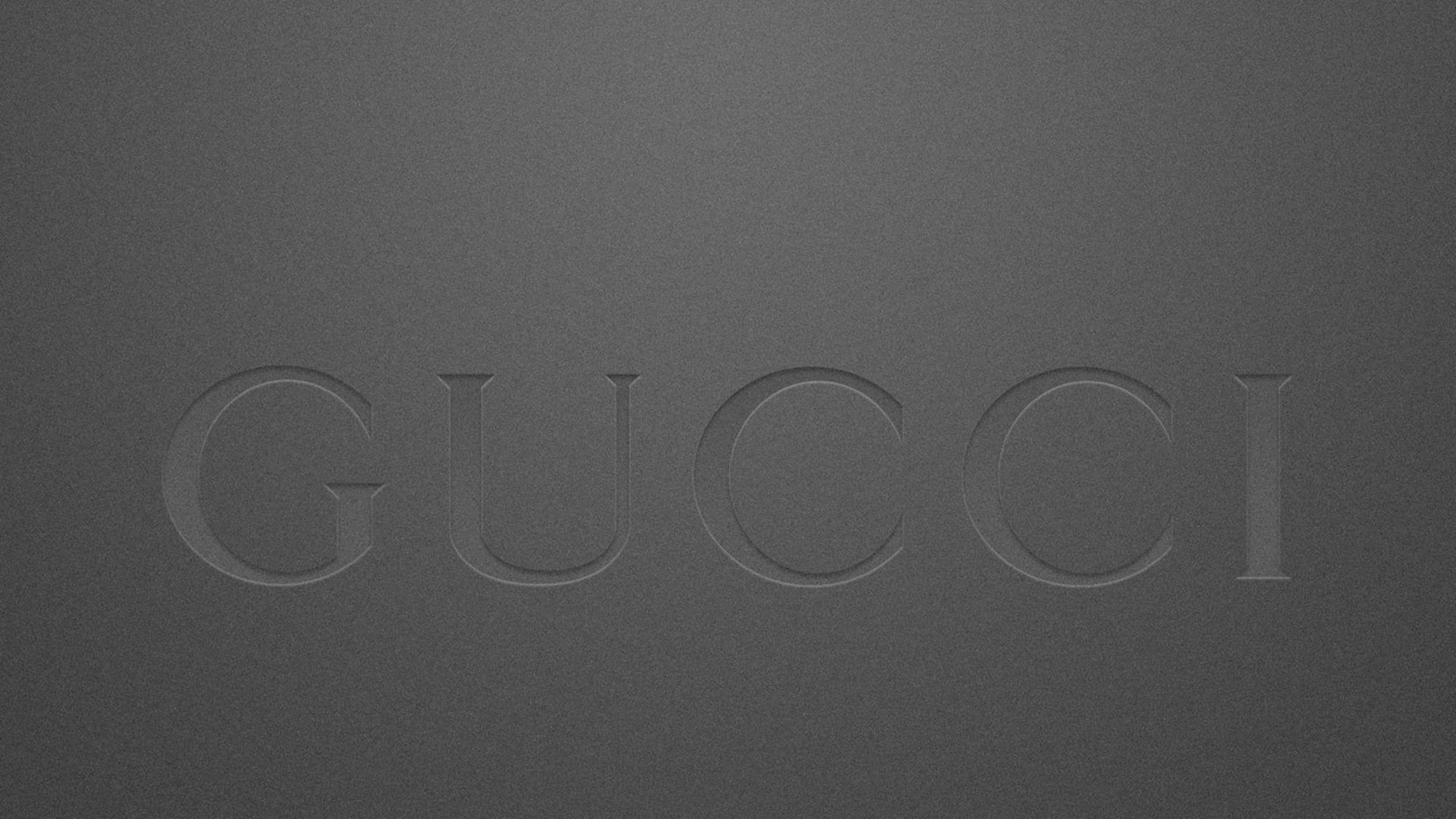 壓紋灰色Gucci標誌4K 壁紙 — GUCCI 這個字以極簡的單色風格微妙地壓印在有紋理的深灰色表面上。