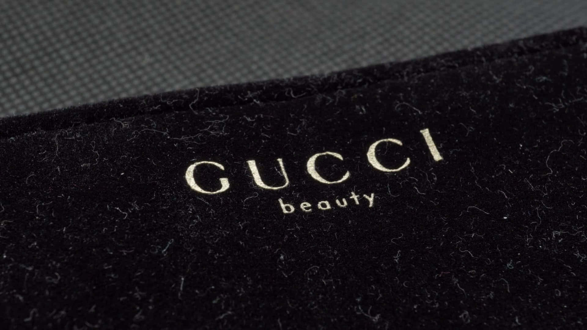 Gucci beauty標誌在黑色天鵝絨布料上，帶紋理灰色背景。
