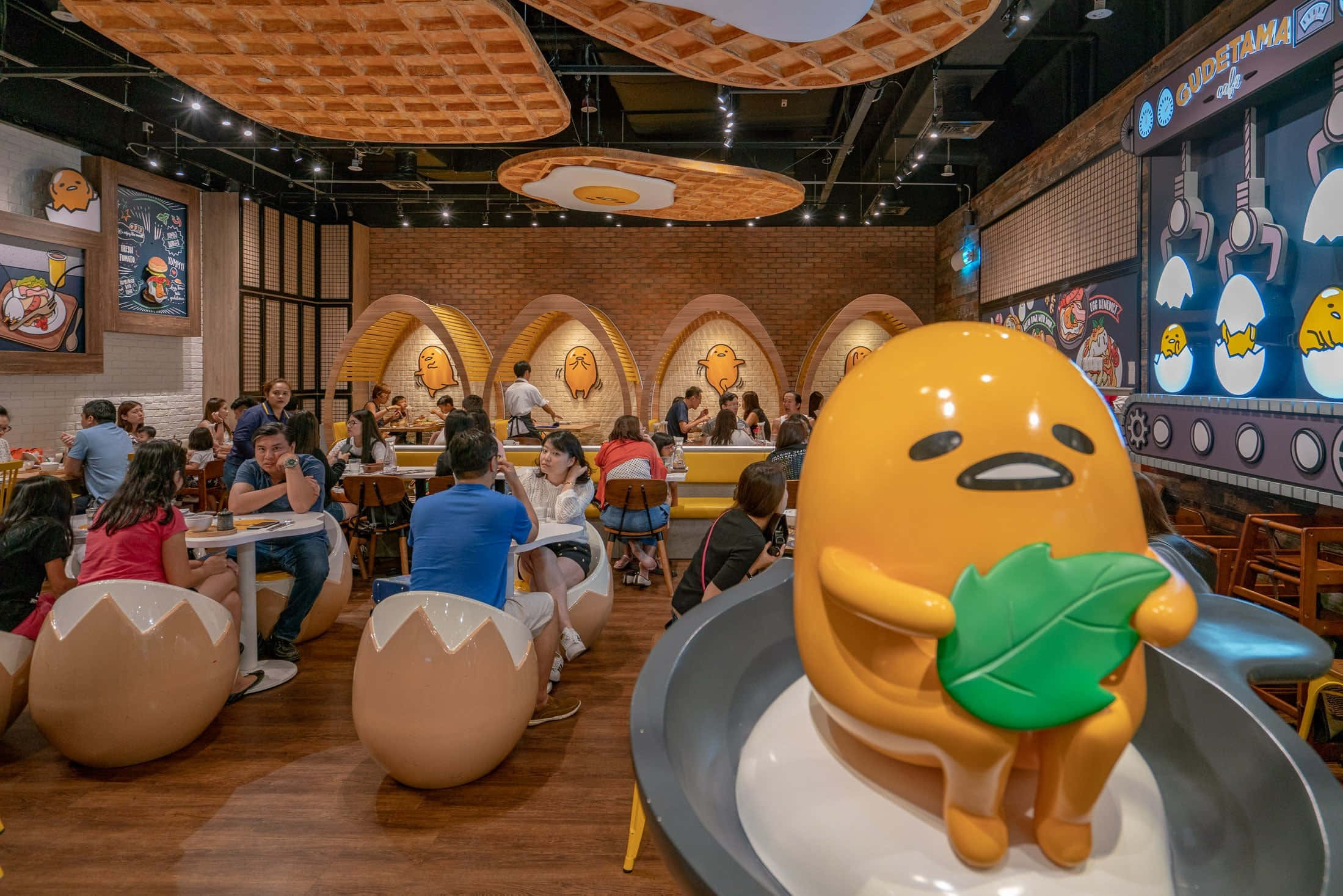 趁Gudetama還在，趕快收藏吧！ 壁紙 — 充滿活力的 Gudetama 主題餐廳，顧客坐在蛋形椅子上，上方是窩夫紋理的天花板。