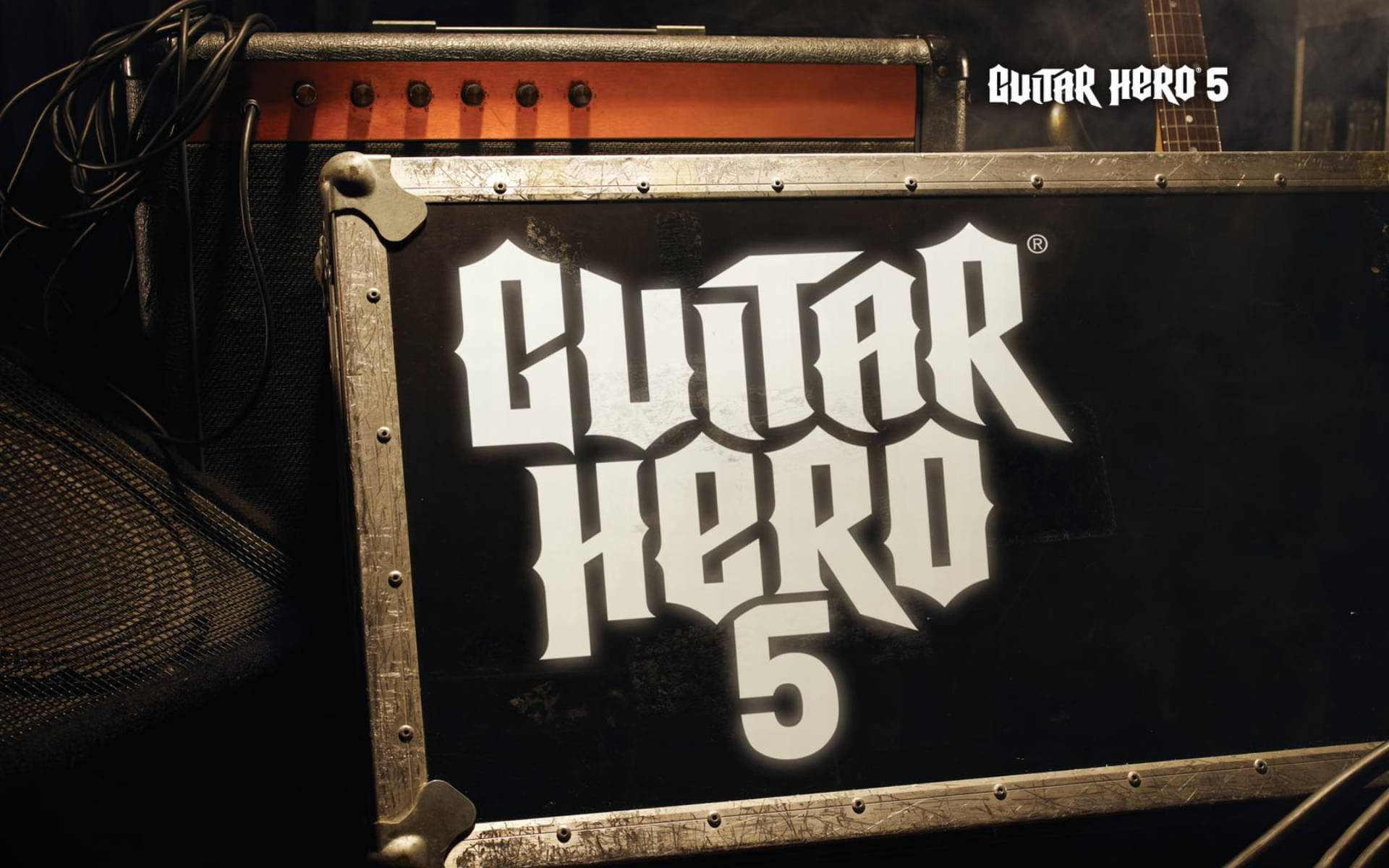 Guitar Hero 5樂隊設備海報 壁紙 — Guitar Hero 5 遊戲盒的特寫，黑色背景上有粗體白色標誌，周圍是暖色燈光下的舞台設備。