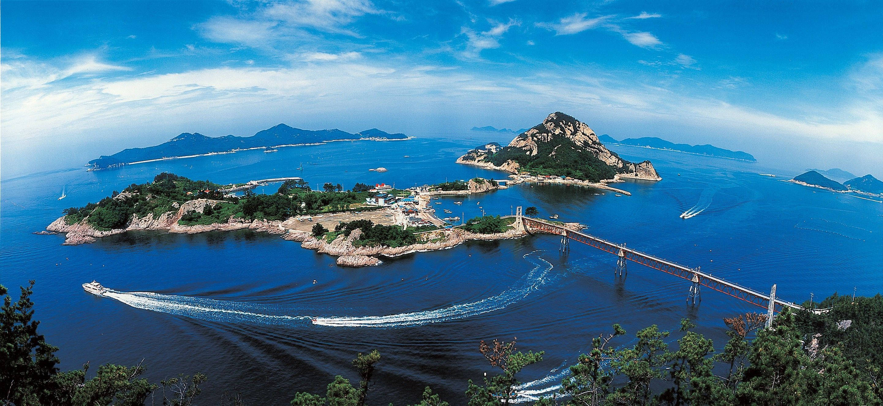 Gunsan島的善宇島 壁紙 — 海岸群島的鳥瞰圖，碧綠的海水，船隻飛馳，一條長橋連接崎嶇的綠色島嶼，天空湛藍。