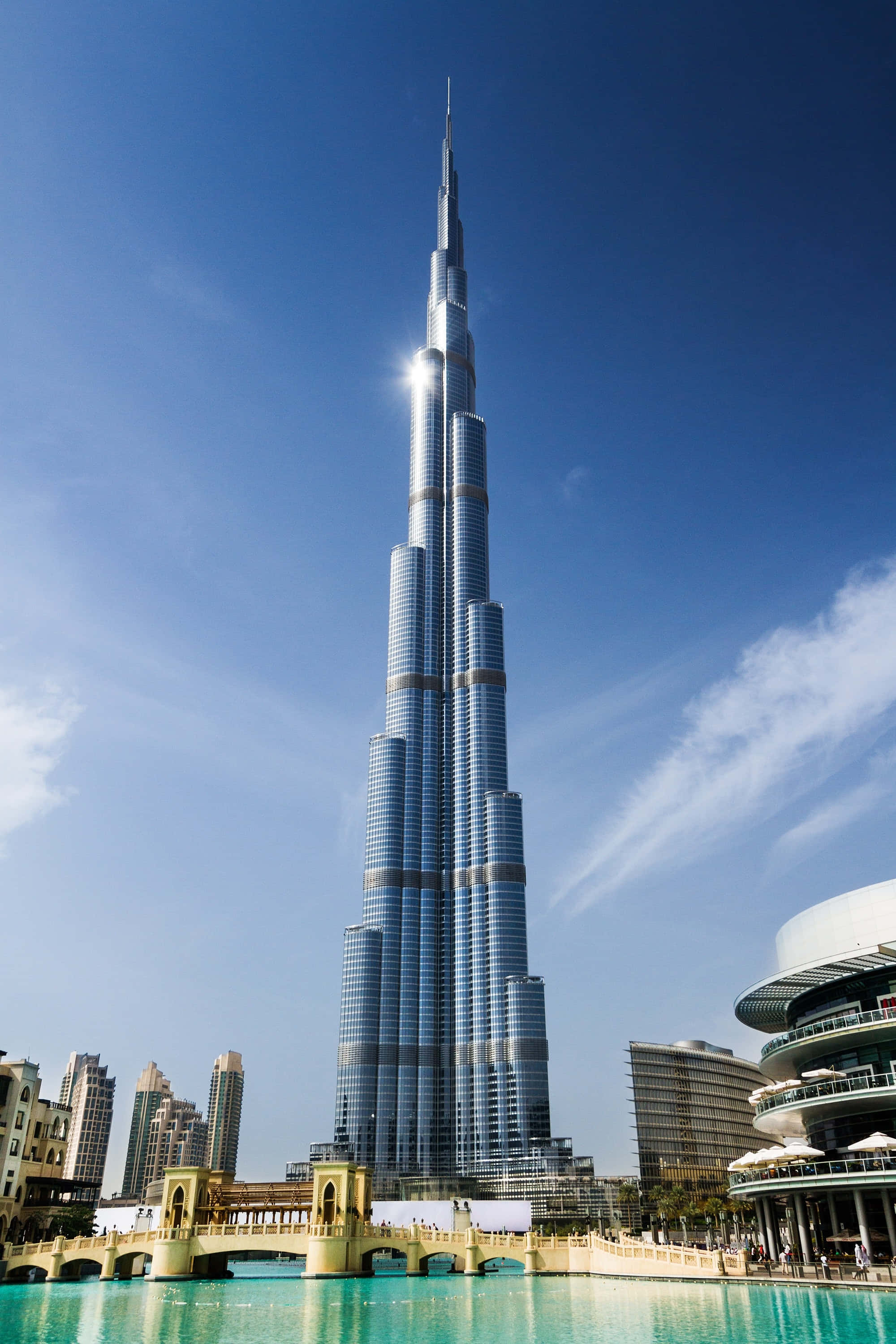 Burj Khalifa 桌布 壁紙 — 哈利法塔在清澈藍天和縷縷白雲下，聳立於碧綠色的泳池之上。
