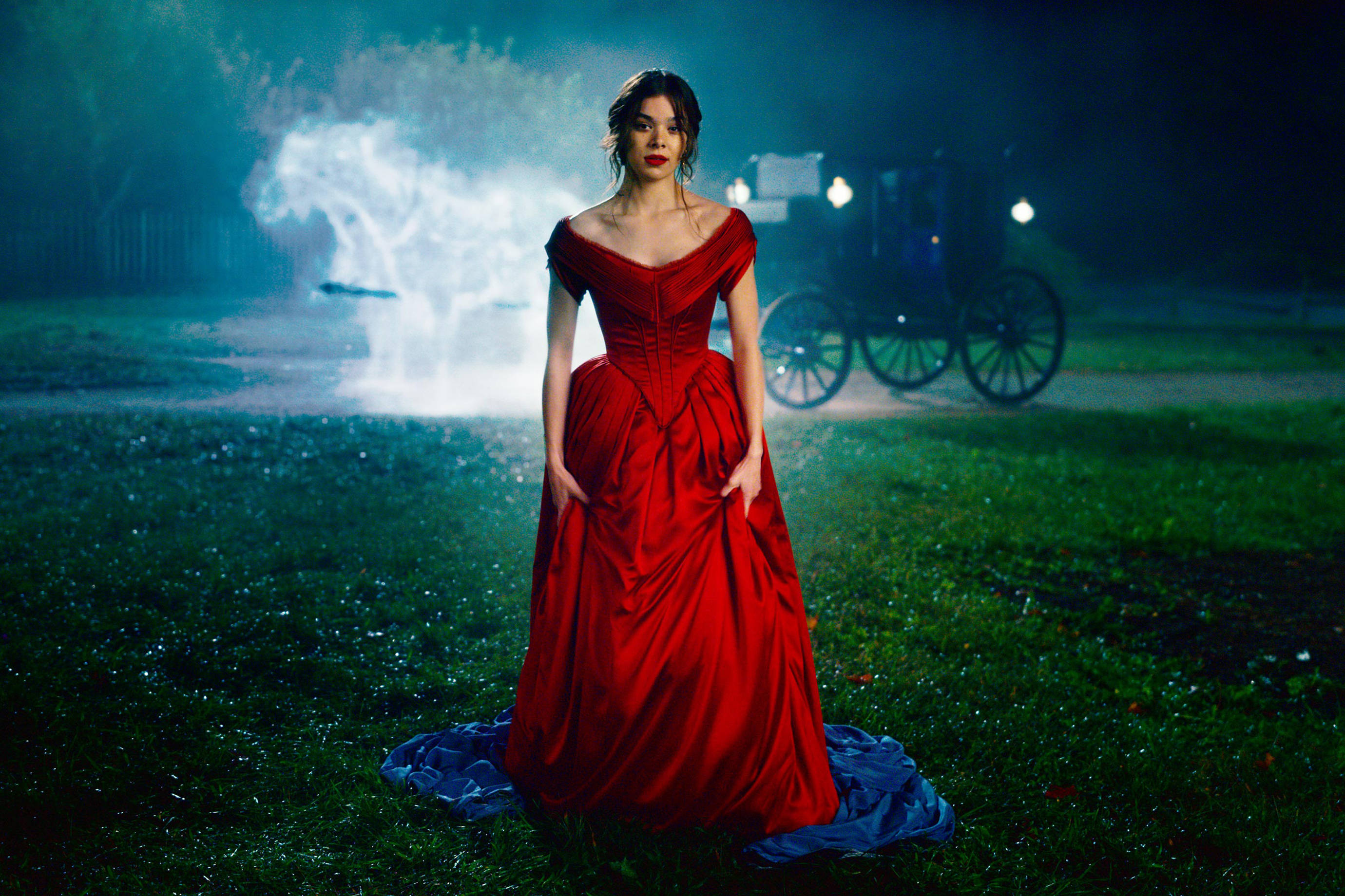 Hailee Steinfeld《Dickinson》紅裙造型 壁紙 — 一位身穿搶眼紅色長裙的女性獨自站在夜晚的草地上，身後有發光的薄霧和一輛馬車。
