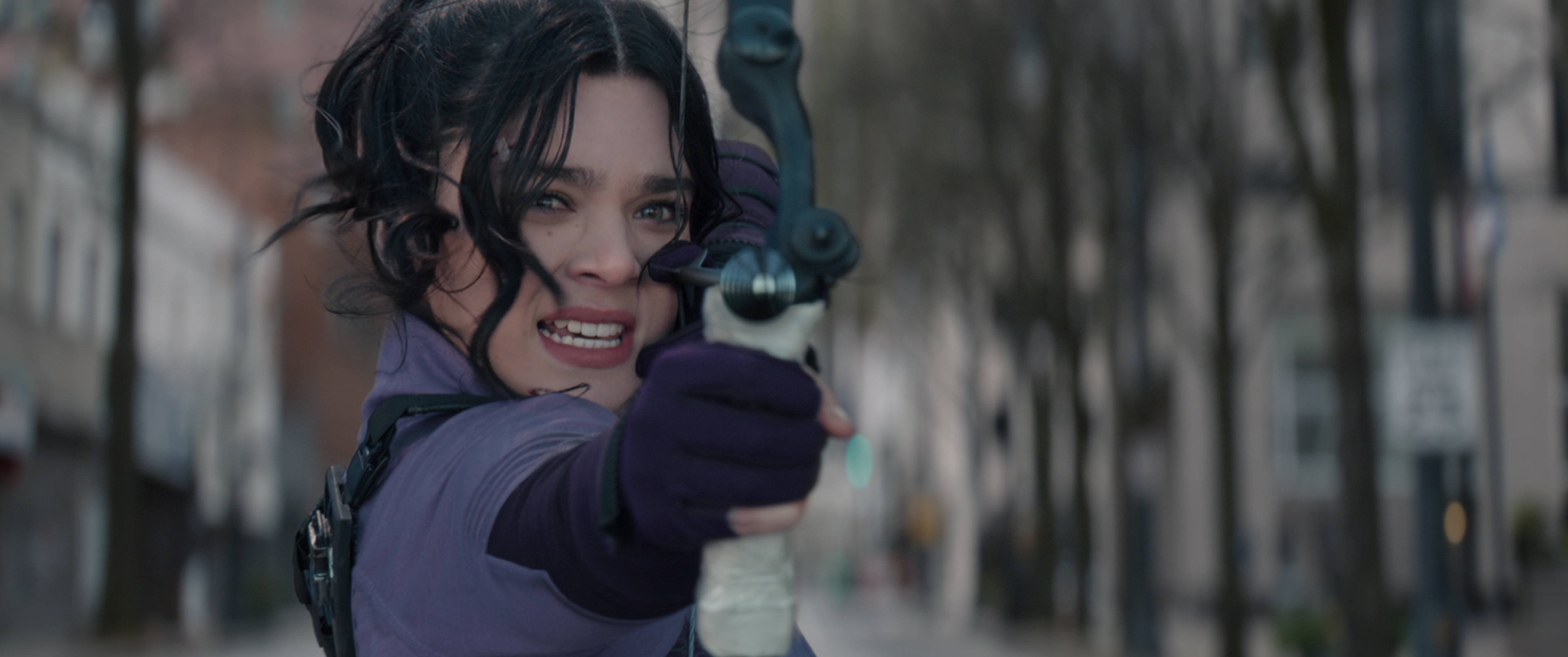 Hailee Steinfeld《Hawkeye》凱特·比希普 壁紙 — 一位堅定的深色頭髮女子，沿著模糊的城市街道專注地瞄準弓箭。