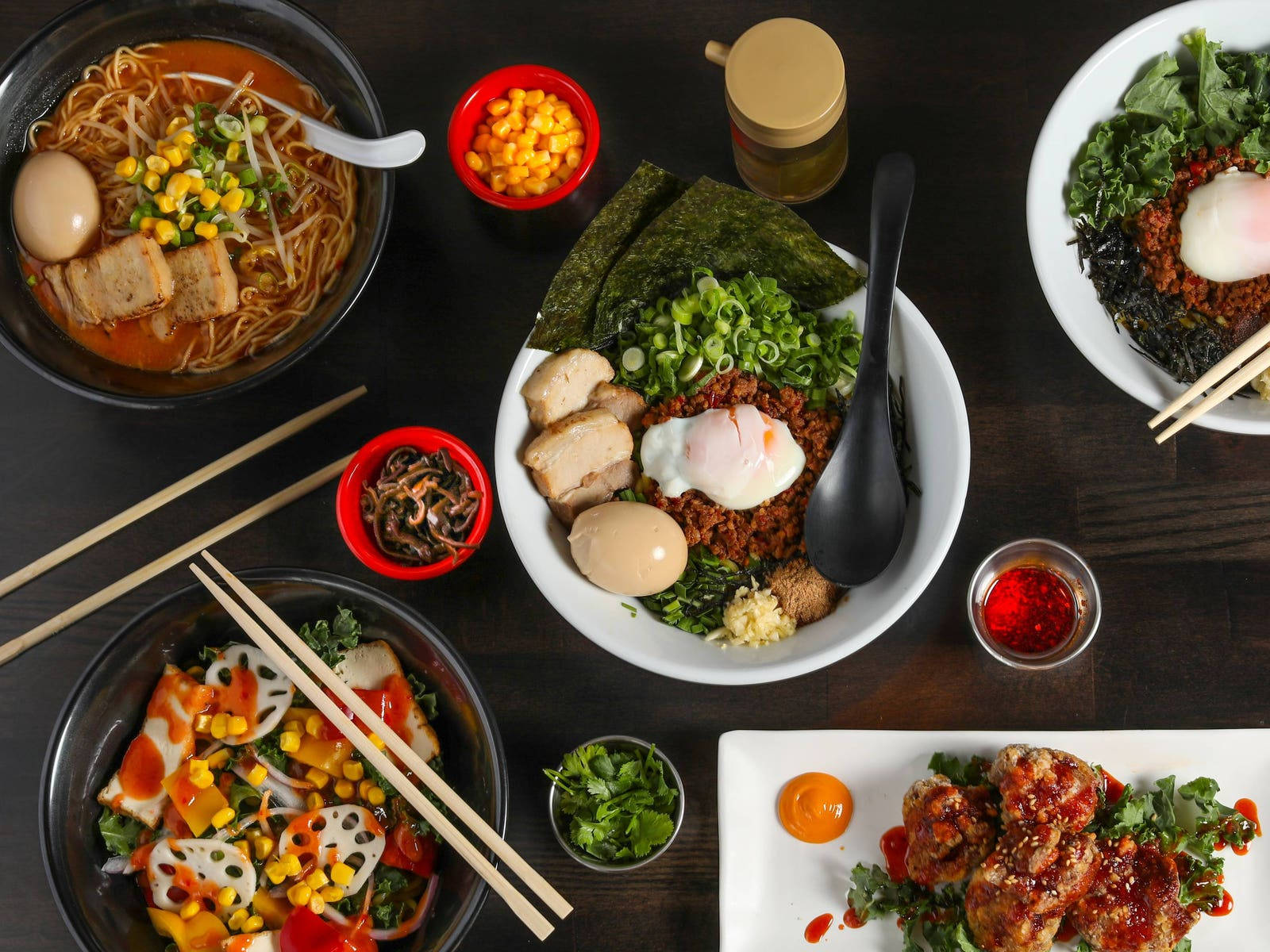 Hakata拉麵日本料理 壁紙 — 從上方俯瞰深色木桌上色彩繽紛的亞洲菜餚，包括拉麵、石鍋拌飯和辣雞。