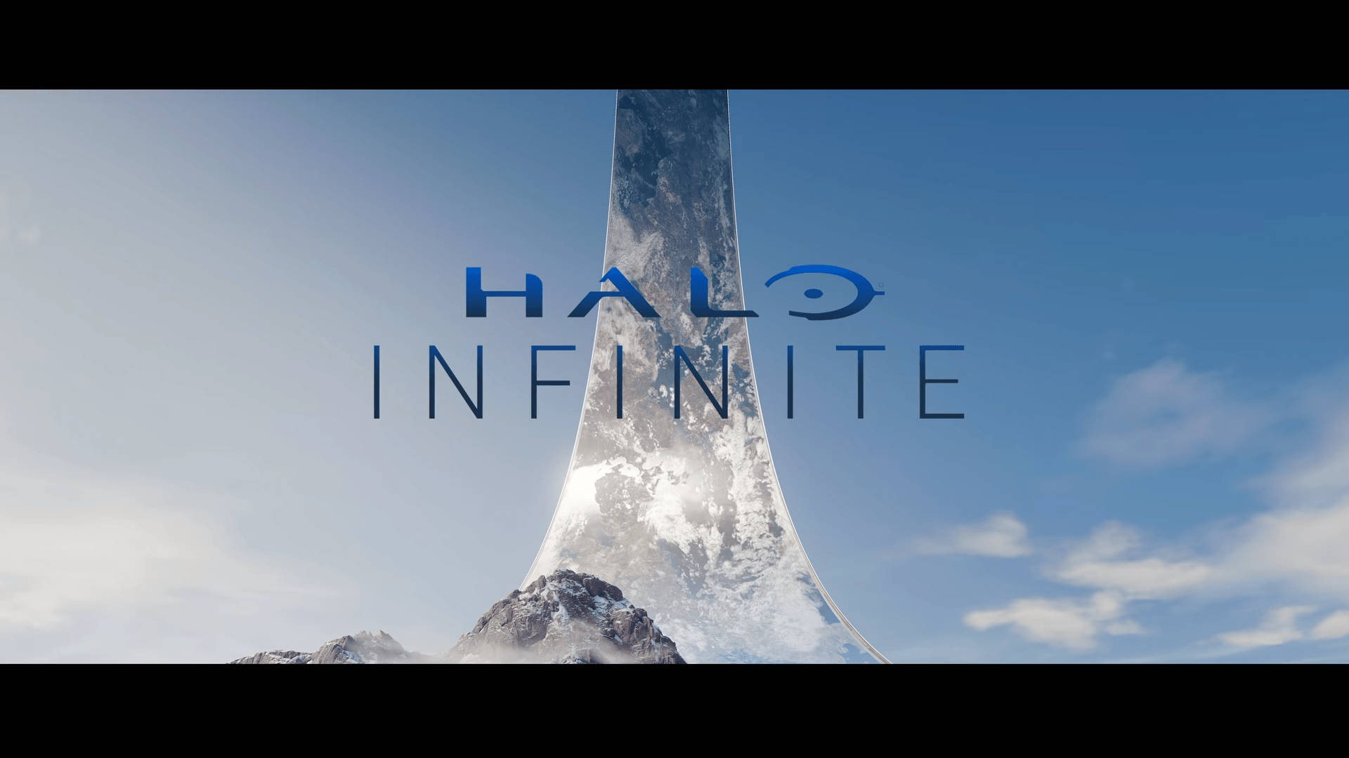 Halo Infinite 白塔 壁紙 — 一個巨大的積雪環狀結構從山頂升起，在晴朗的藍天下，Halo Infinite 標誌漂浮在上方。