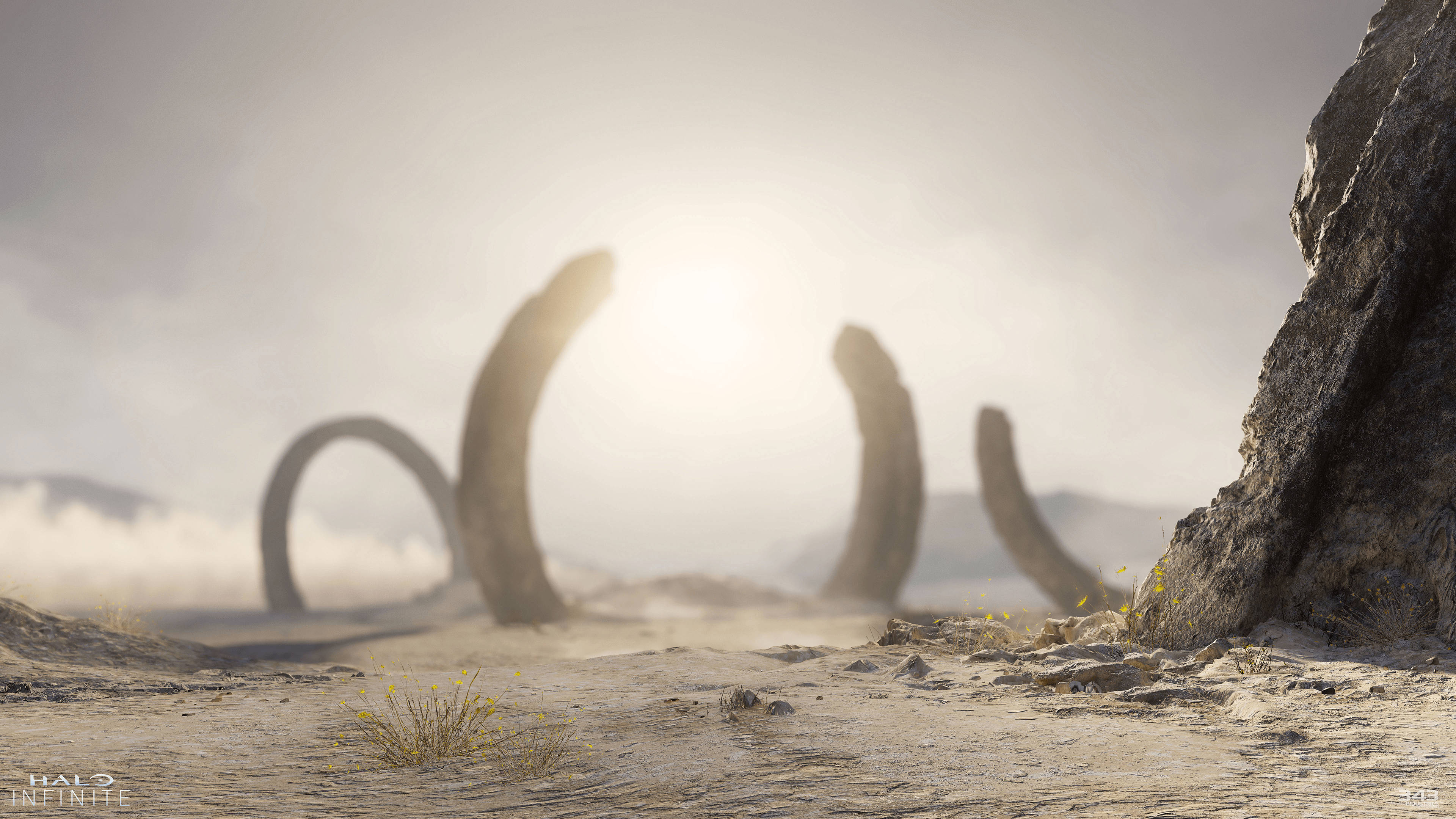 《Halo Infinite》破碎的澤塔環 壁紙 — 古老的環形結構從塵土飛揚的外星景觀中升起，在朦朧的太陽下，岩石地形和稀疏的黃色花朵。
