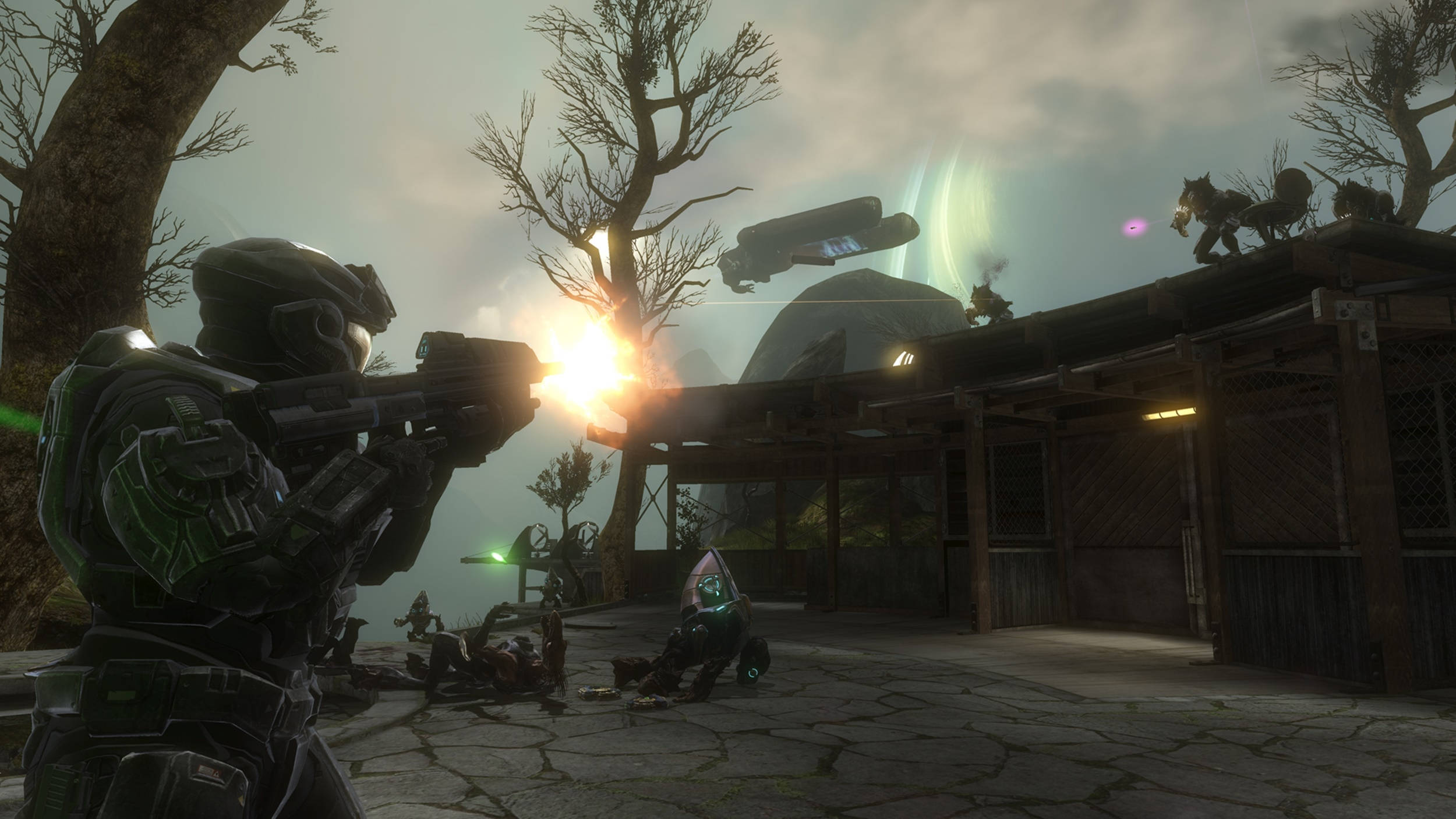Halo：達陣截圖 壁紙 — 一名身穿綠色盔甲的士兵在陰天、外星飛船盤旋的天空下，向木結構附近的敵人開火。