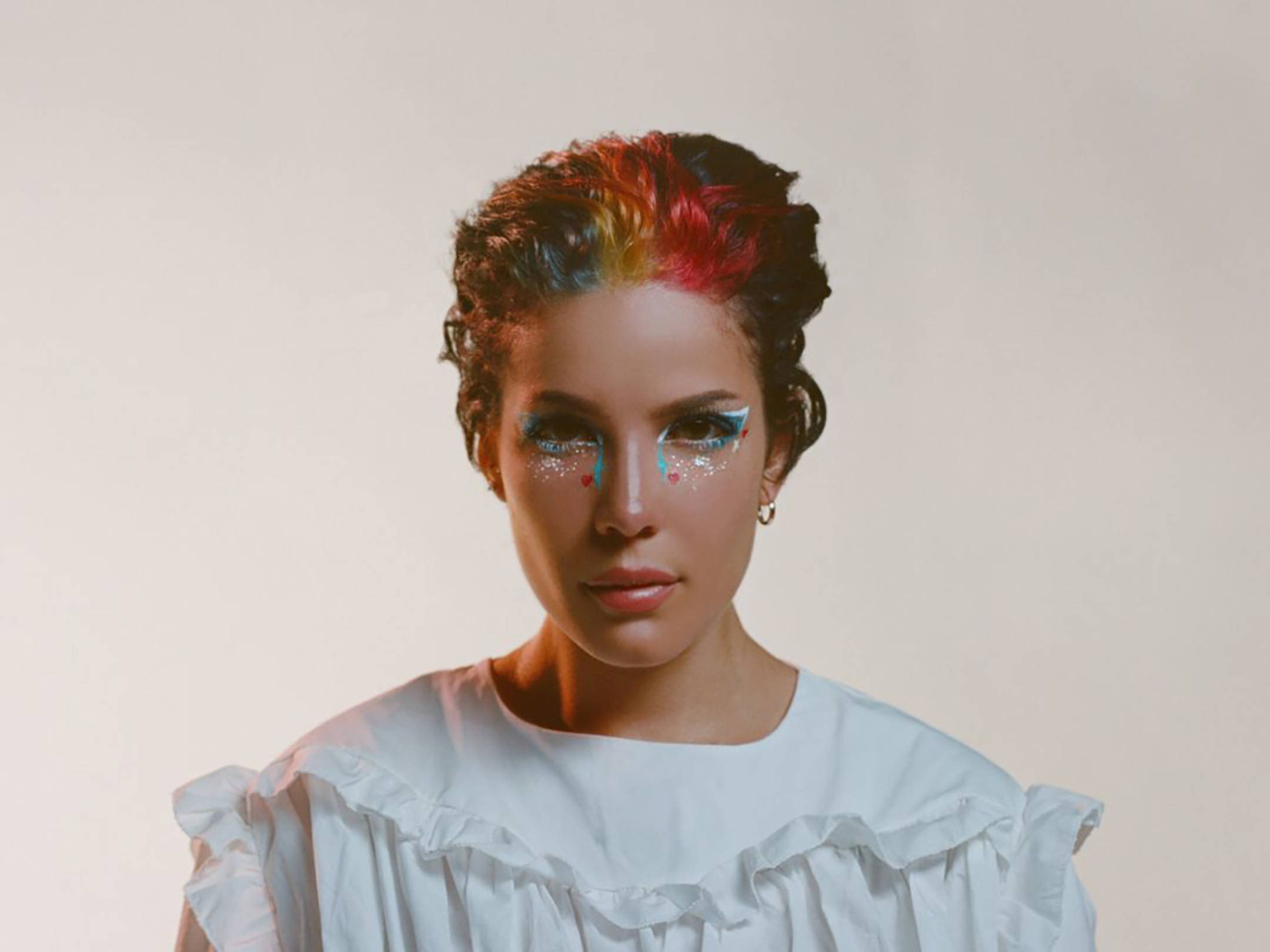 Halsey《Manic》專輯造型 壁紙 — 一位擁有彩虹色頭髮和閃亮藍色眼妝的女性，穿著白色荷葉邊襯衫，直視鏡頭。