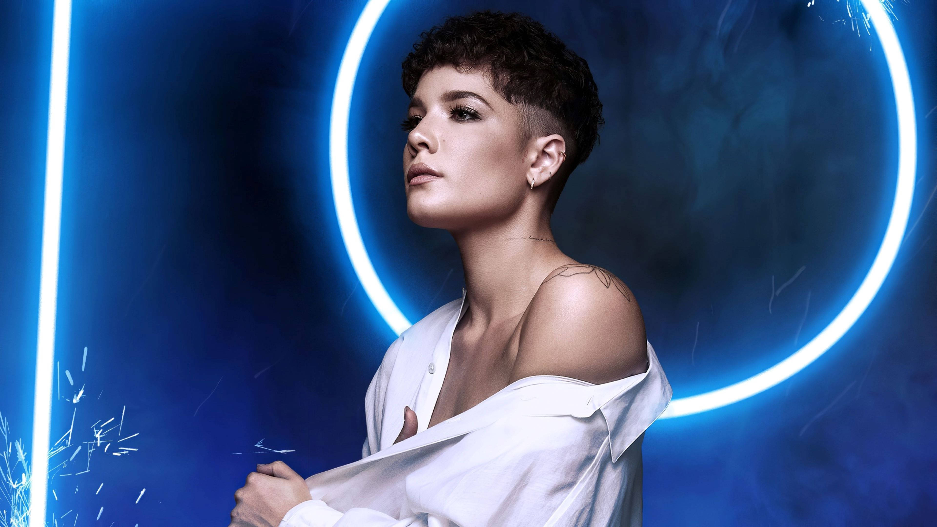 Halsey 搭配捲髮男孩髮型 壁紙 — 一位短黑髮女性站在藍色霓虹燈光的工作室中，穿著露肩白色襯衫，被發光的圓形燈光和火花所環繞。