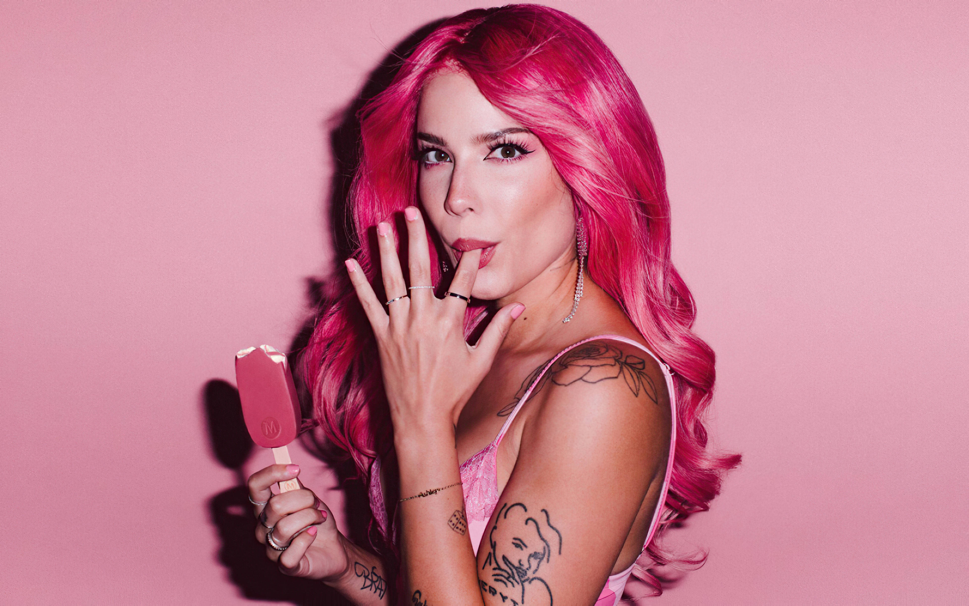 Halsey 粉紅甜美風 壁紙 — 一位擁有亮麗粉紅色頭髮和紋身的女性，在純粉紅色背景前拿著一支粉紅色冰棒。