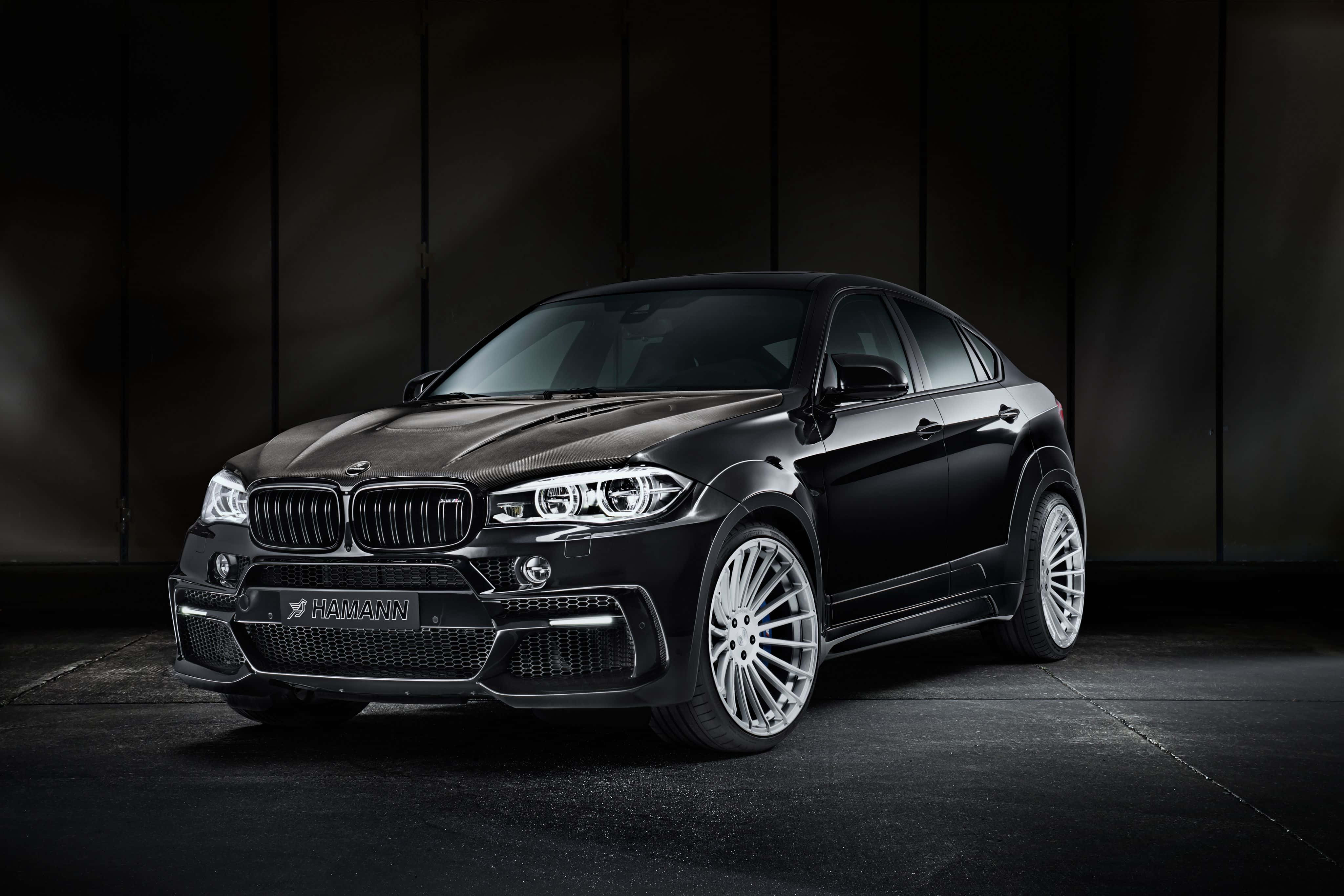 Bmw X6 桌布 壁紙 — 一架由Hamann改裝的黑色寶馬X6 M，在戲劇性的影樓燈光下，以深色紋理牆壁為背景，型格地佇立。
