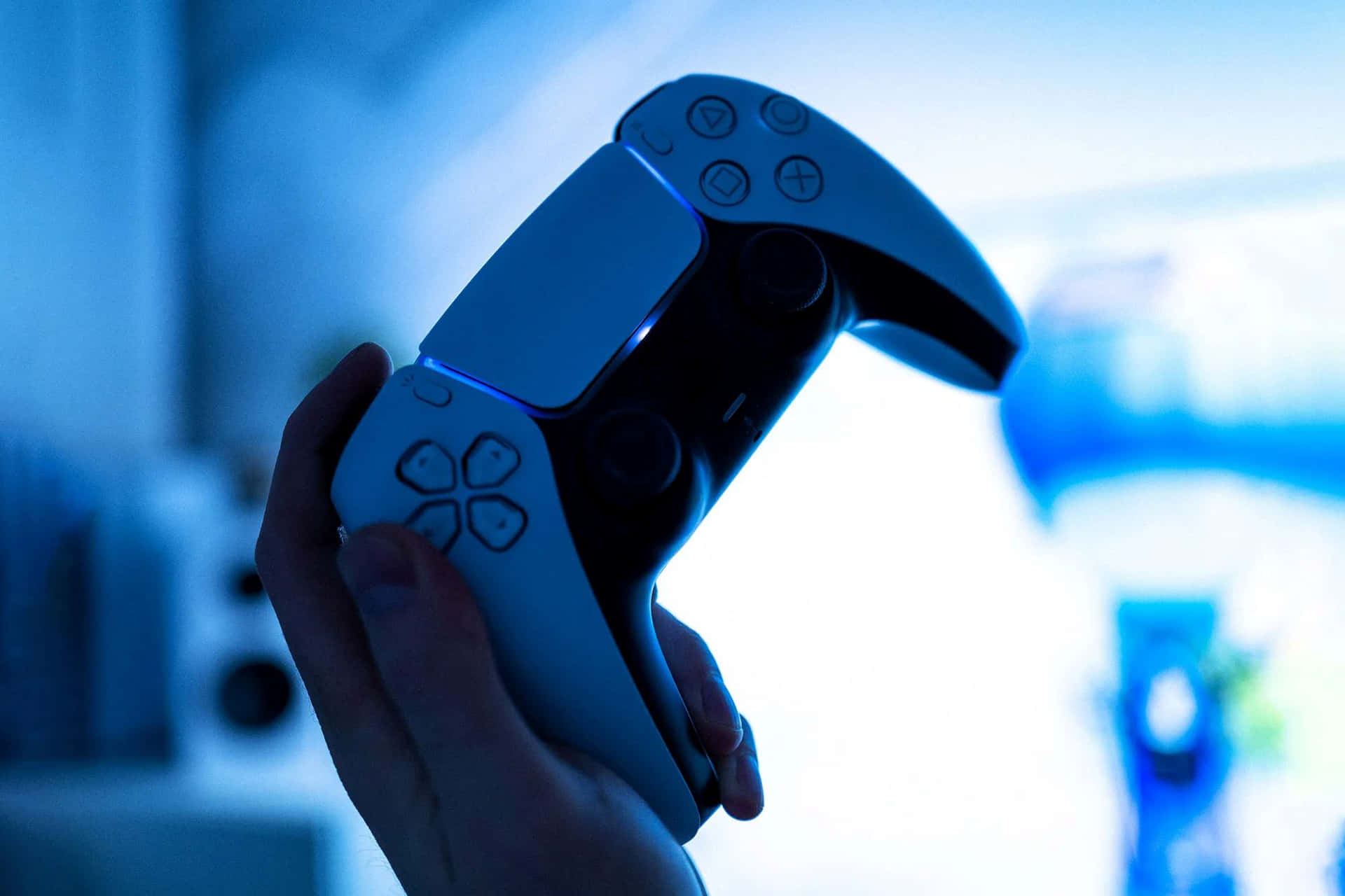  壁紙 — 一隻手握住浸浴在冷藍光中的PlayStation 5控制器，背景是模糊的遊戲畫面。