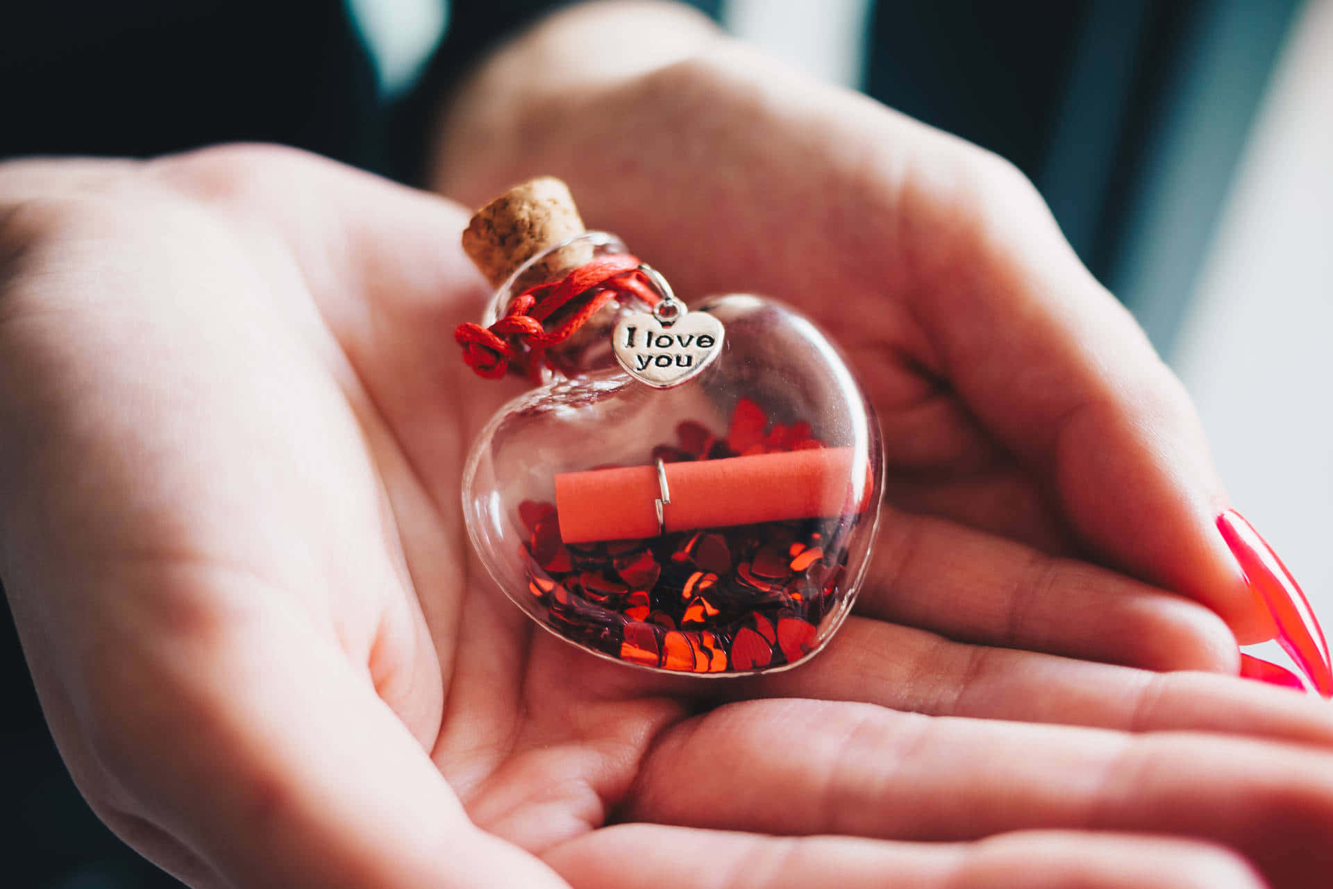  壁紙 — 一隻手捧著一個心形玻璃瓶，裡面裝滿紅色閃粉和一卷寫著「我愛你」的字條。