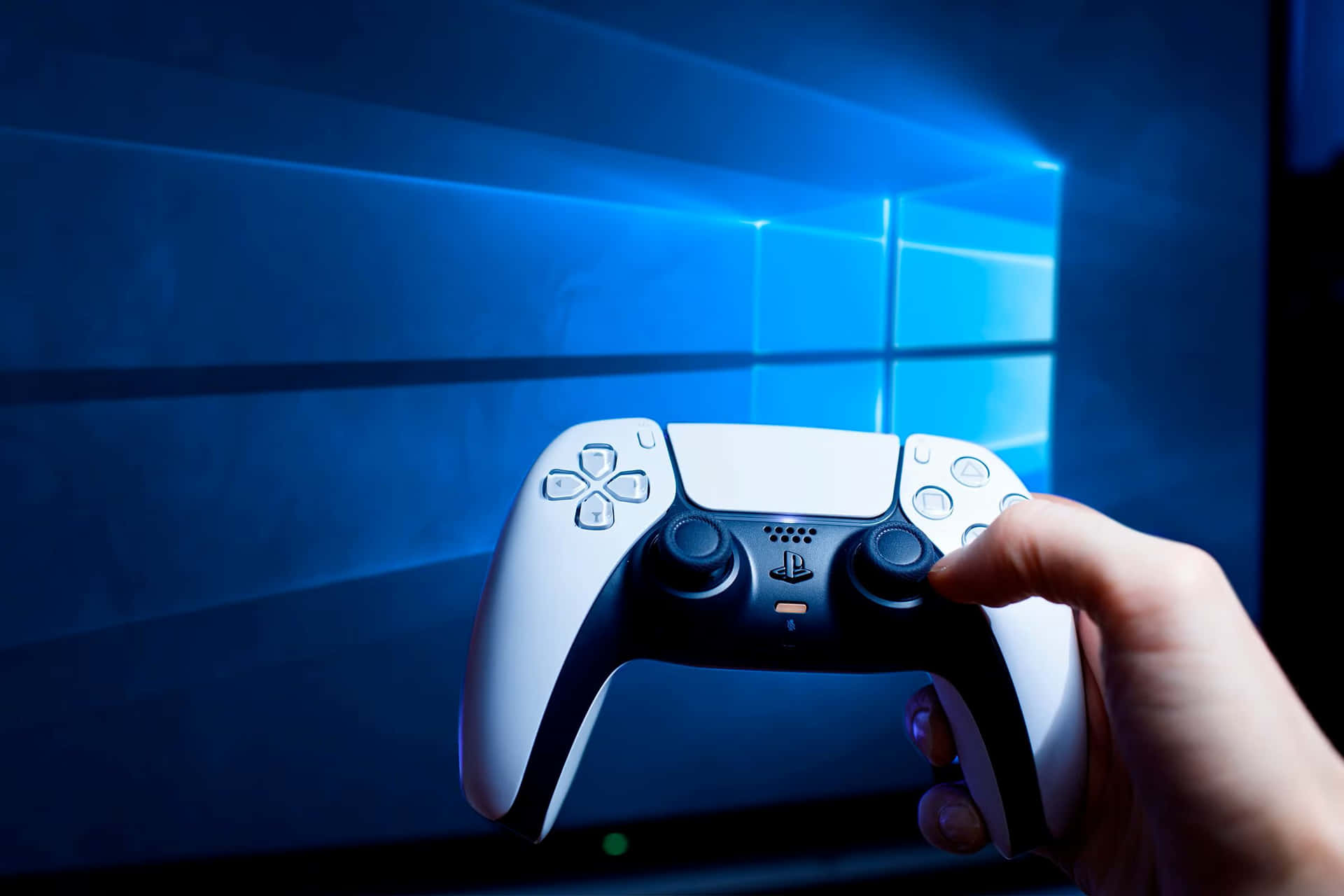  壁紙 — 一隻手在發光的藍色 Windows 11 桌面背景前握著一個白色 PlayStation 5 控制器。