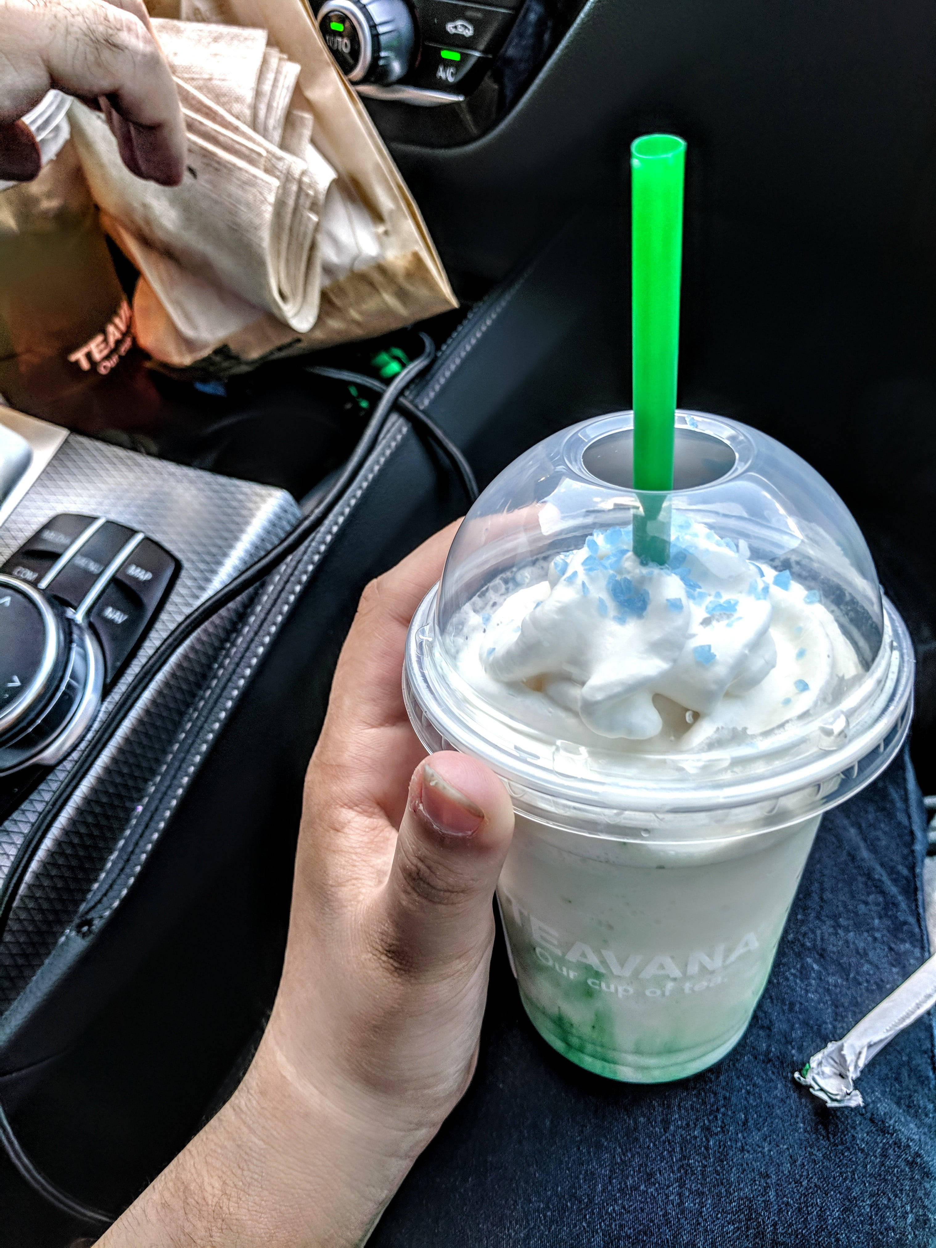 手在車內拿著一杯有忌廉和藍色糖粒的Teavana冰茶。