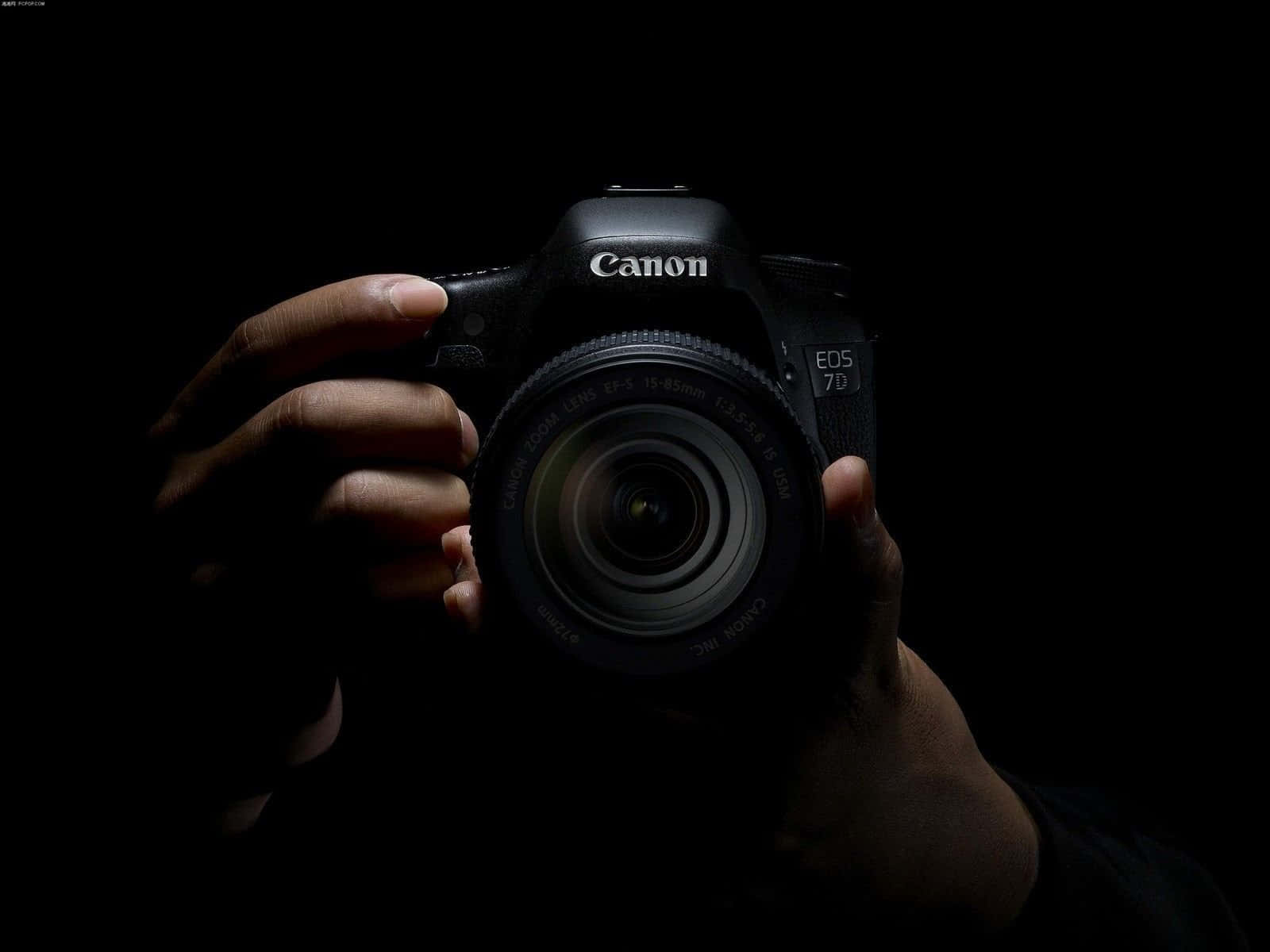 Cameraman 桌布 壁紙 — 一隻手在純黑色背景上，以戲劇性的聚光燈照射下，拿著一部黑色的Canon EOS 7D DSLR相機。