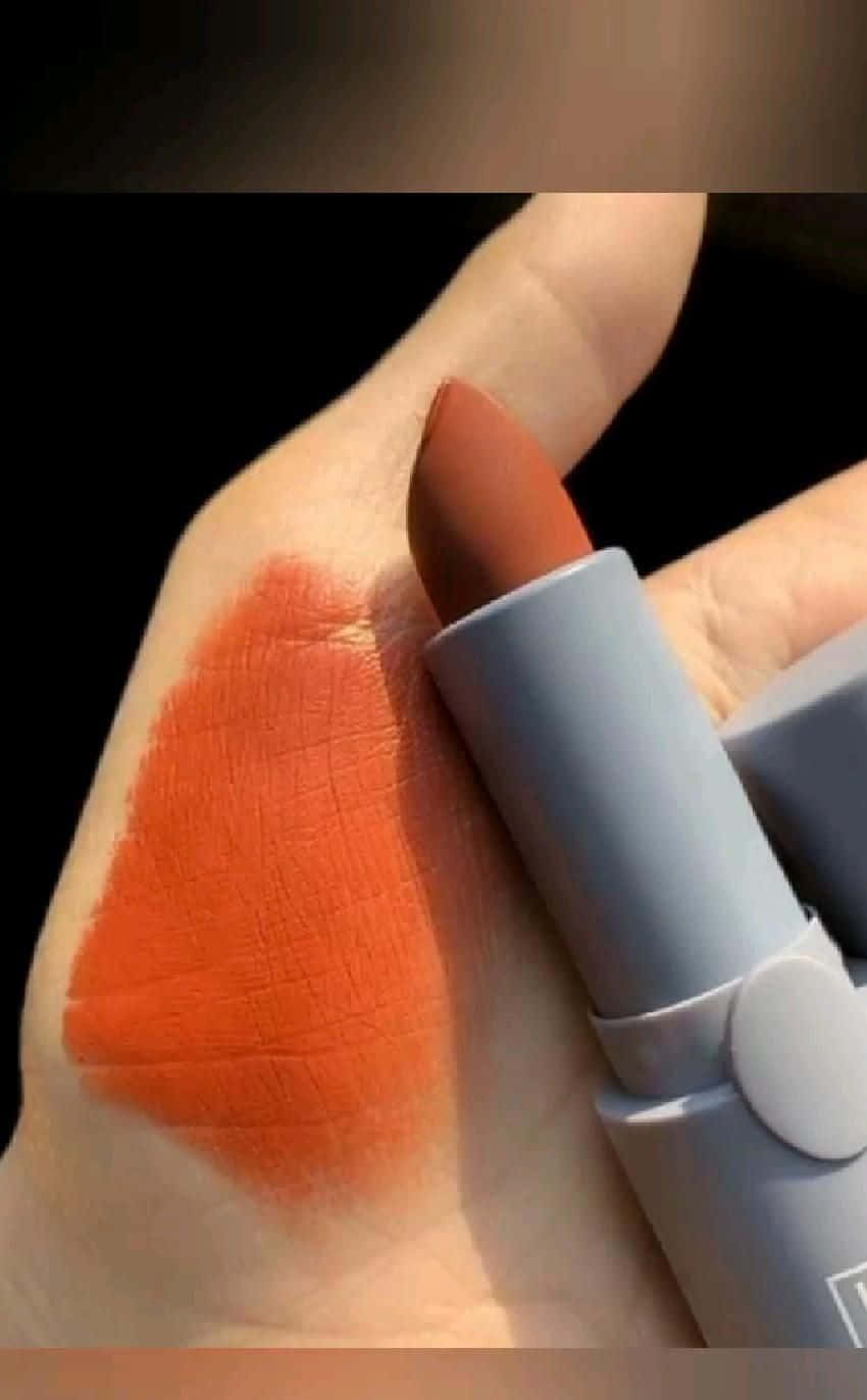 lipstick 桌布 壁紙 — 一隻手拿著一支啞光橙色唇膏，在手背上大膽地試色，背景為深色。