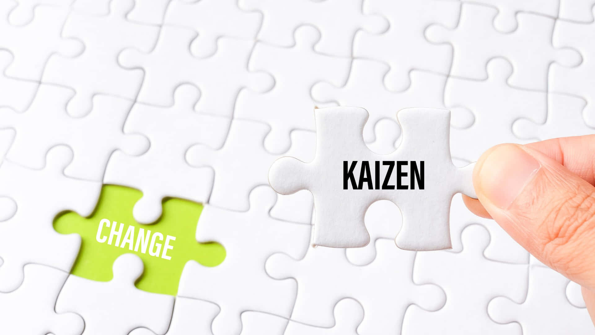  壁紙 — 一隻手將一塊標有「KAIZEN」的白色拼圖塊放入一個白色拼圖中，下方有一塊標有「CHANGE」的綠色拼圖塊。