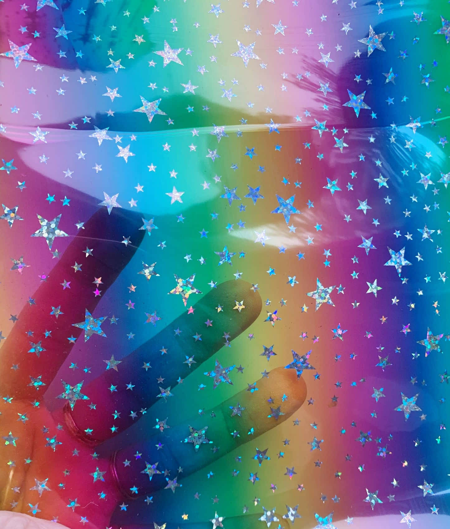 Rainbow Glitter 桌布 壁紙 — 一隻手穿過彩虹色、佈滿星星的半透明表面，營造出夢幻的宇宙效果。