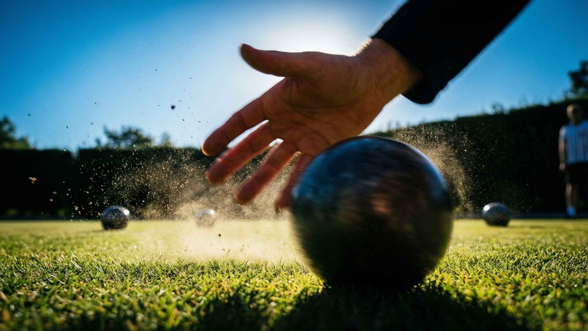 Petanque 桌布 壁紙 — 一隻手將金屬球釋放到充滿活力的綠色草地上，在明亮的陽光下揚起灰塵。