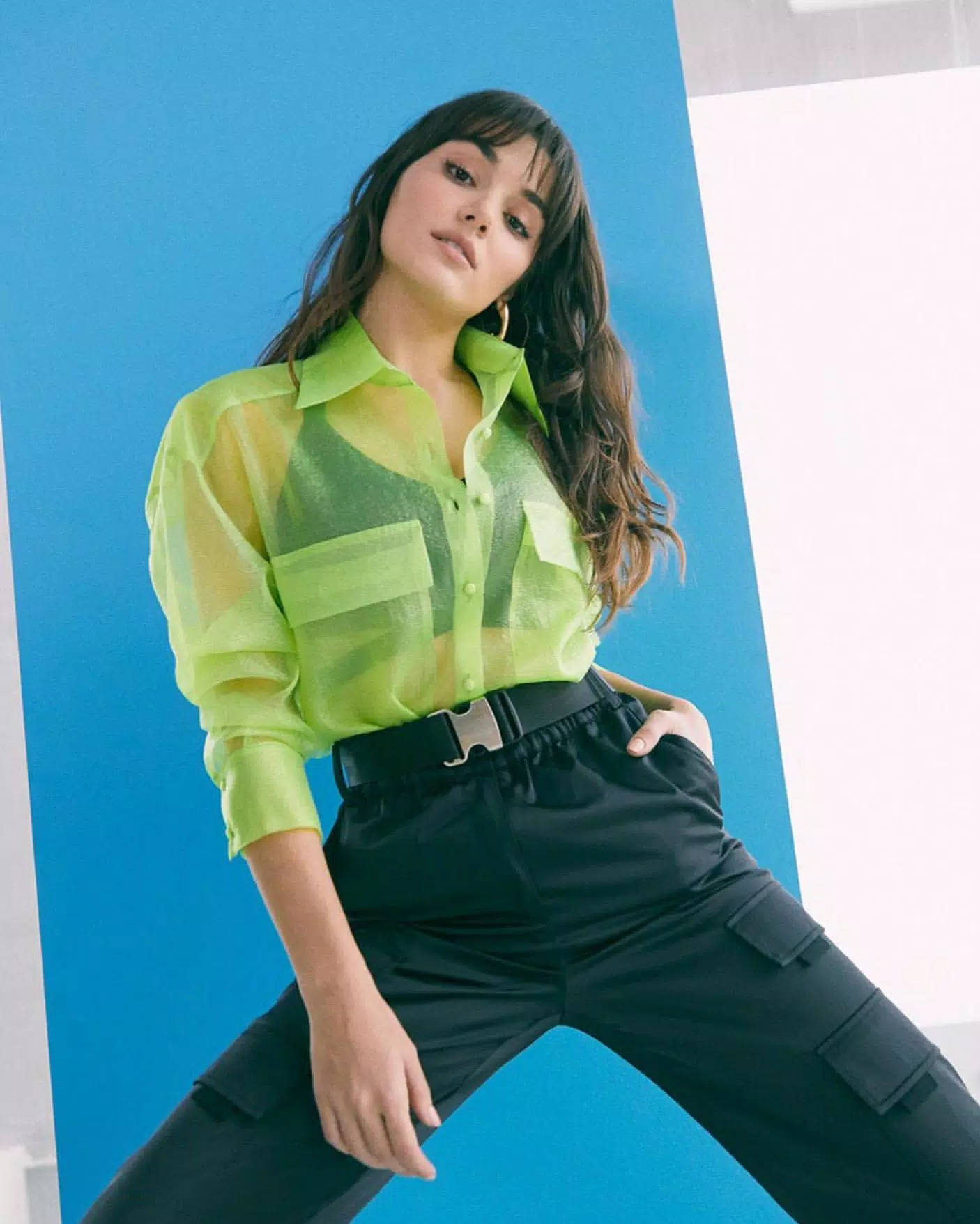 Hande Ercel 時尚寫真 壁紙 — 一位身穿鮮豔螢光綠色透視襯衫和黑色工裝褲的女性，在醒目的藍白幾何背景前自信地擺姿勢。