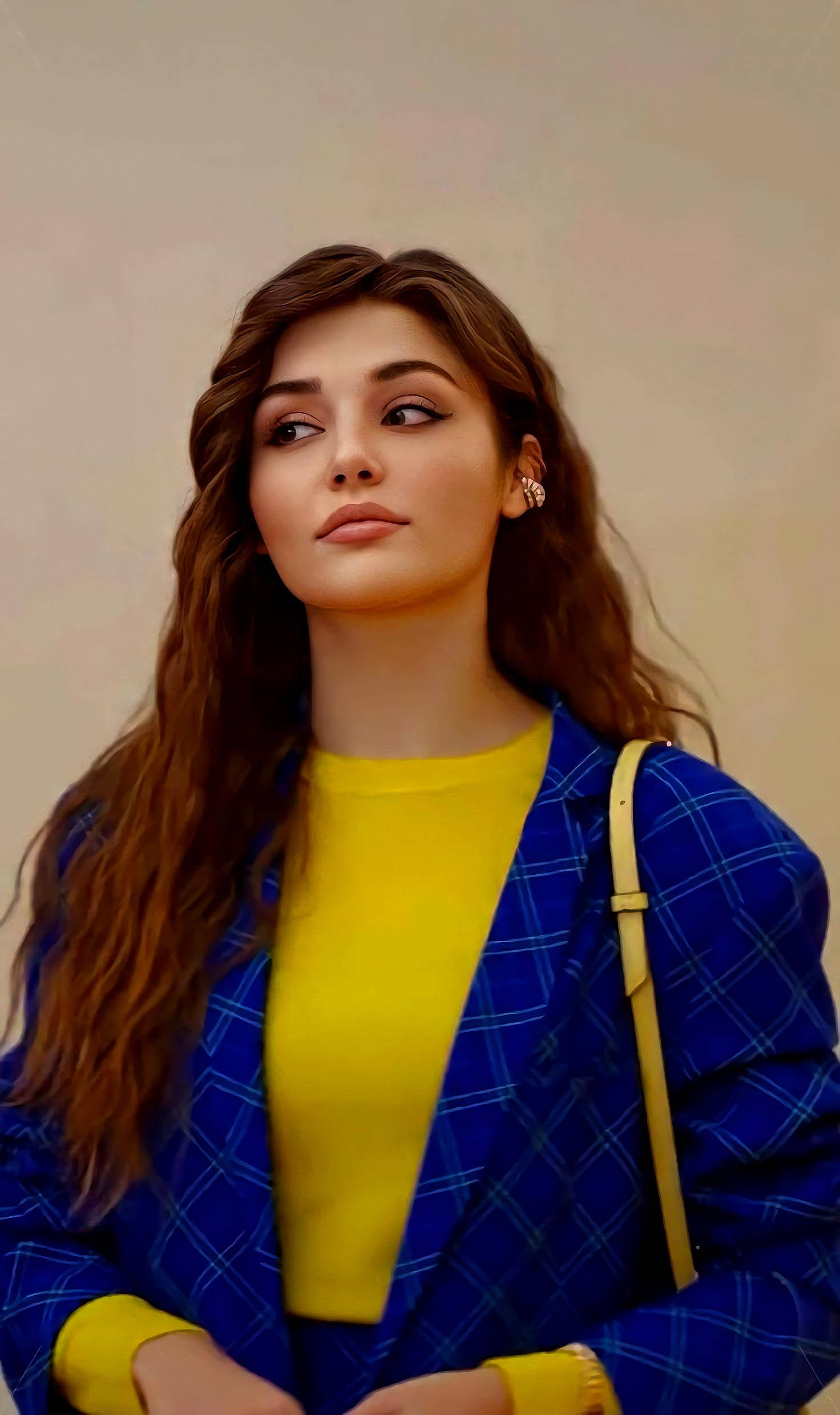 Hande Ercel 側目凝視 壁紙 — 一位長髮棕色年輕女性身穿藍色格紋西裝外套配黃色上衣，並攜帶米色肩背包。