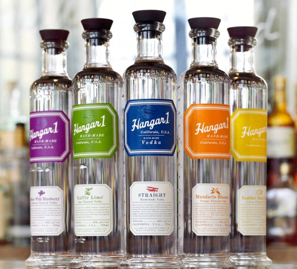 Hangar 1 蒸餾酒系列伏特加 壁紙 — 五個帶有彩色標籤的 Hangar 1 伏特加酒瓶排成一排放在吧枱上。