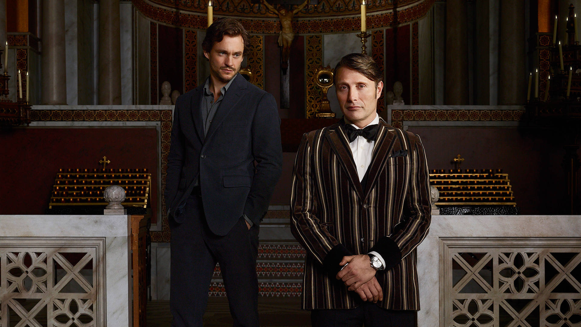 《 Hannibal 》「殺人丈夫」二人組 壁紙 — 兩名身穿正裝的男子自信地站在一個裝飾華麗、燭光閃爍的教堂內部，內有大理石祭壇和紅色牆壁。