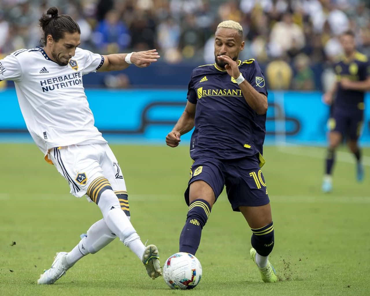 Hany Mukhtar 對決LA Galaxy Martin Caceres 壁紙 — 兩名足球運動員在明亮的日光下，在充滿活力的綠色球場上激烈爭球。