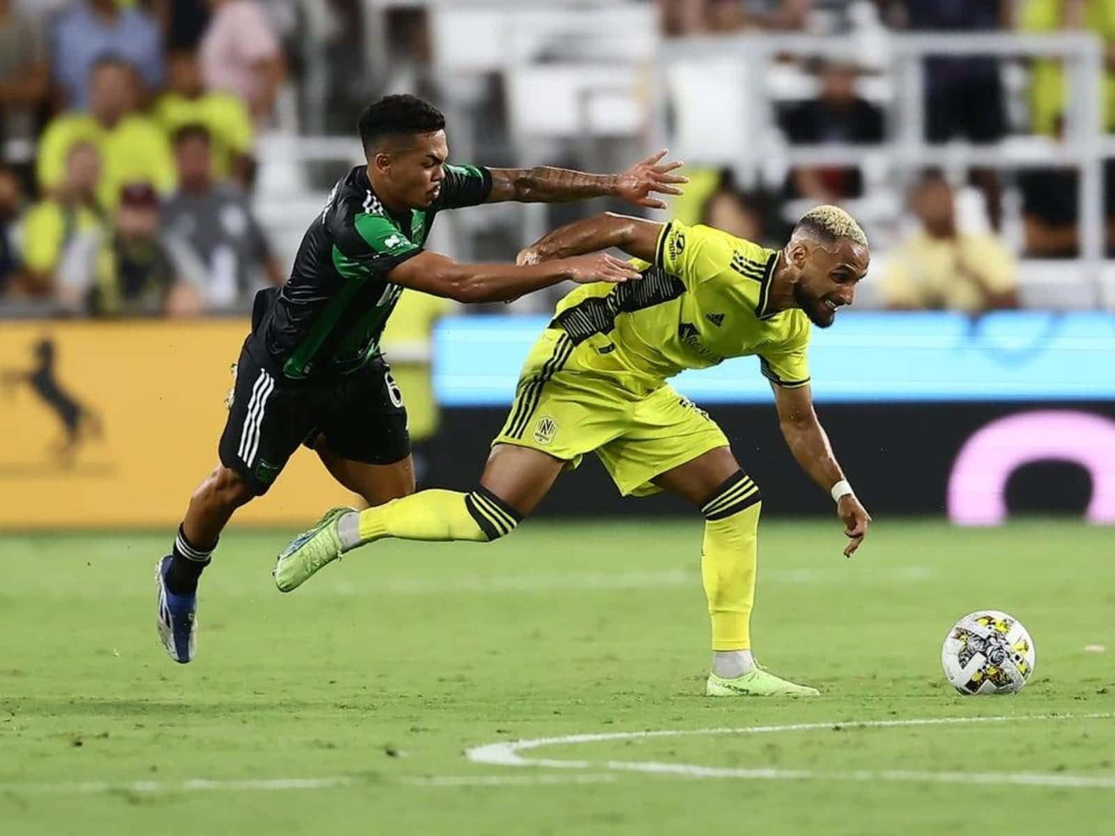 Hany Mukhtar 追逐球對抗奧斯汀FC 壁紙 — 兩名足球運動員在球場燈光下，於充滿活力的綠色草地上激烈爭奪球權。