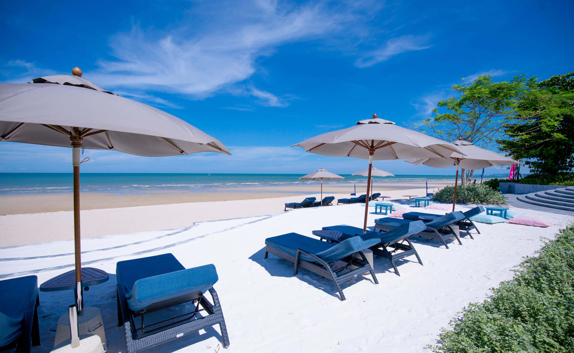Beach Resort 桌布 壁紙 — 豪華藍色躺椅和米色遮陽傘點綴在純淨的白色沙灘上，上方是帶有縷縷白雲的湛藍天空。