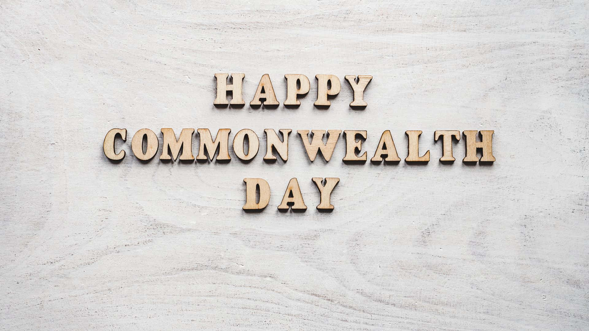 木製字母在淺色紋理背景上拼出 Happy Commonwealth Day。