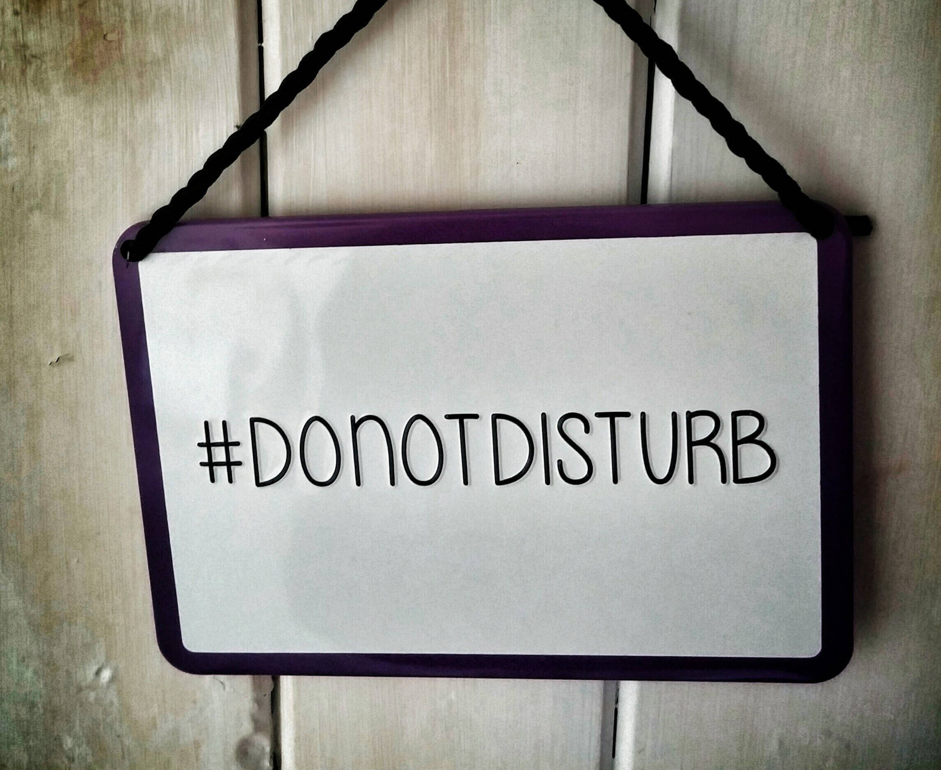 一個帶紫色邊框和「#DONOTDISTURB」的標誌掛在木門上。