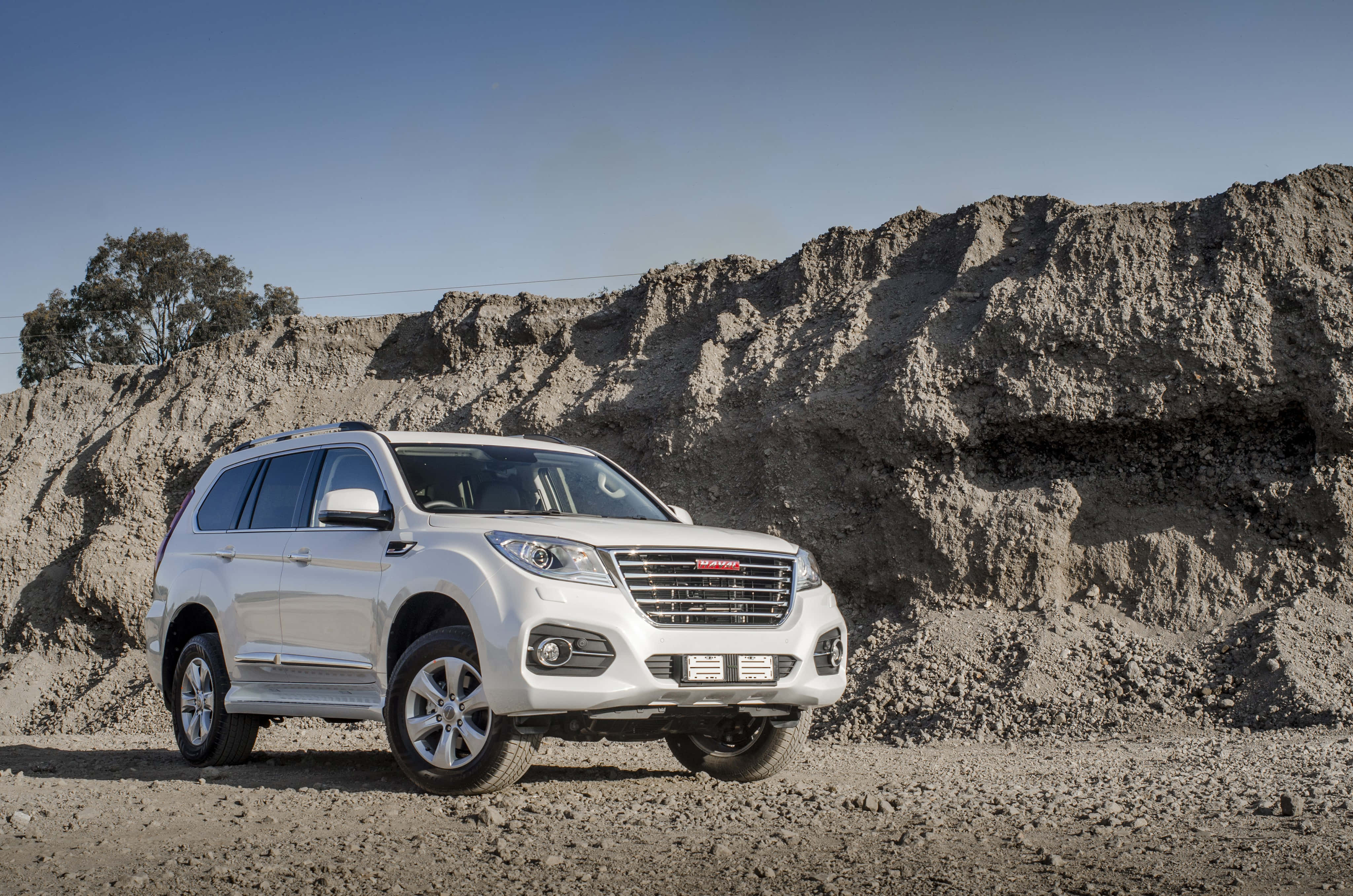 有型嘅 Haval SUV 泊喺戶外 壁紙 — 一輛時尚的銀色SUV在崎嶇地形上，矗立於高聳的土崖前，天空湛藍清澈。