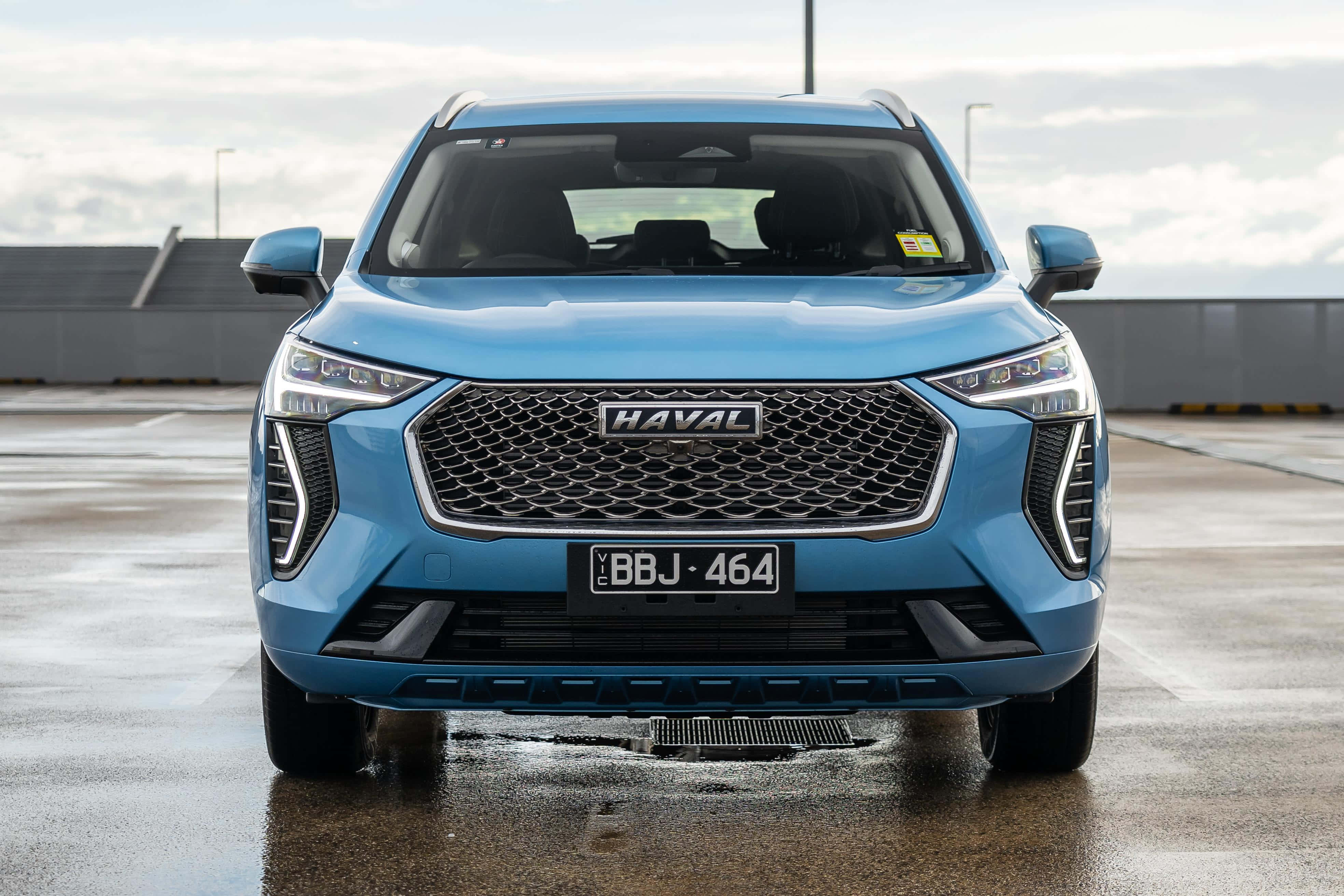流暢現代嘅 Haval SUV 喺廣闊風景中行駛 壁紙 — 一輛時尚的藍色哈弗SUV在潮濕的停車場上向前，天空陰沉，水坑反射。