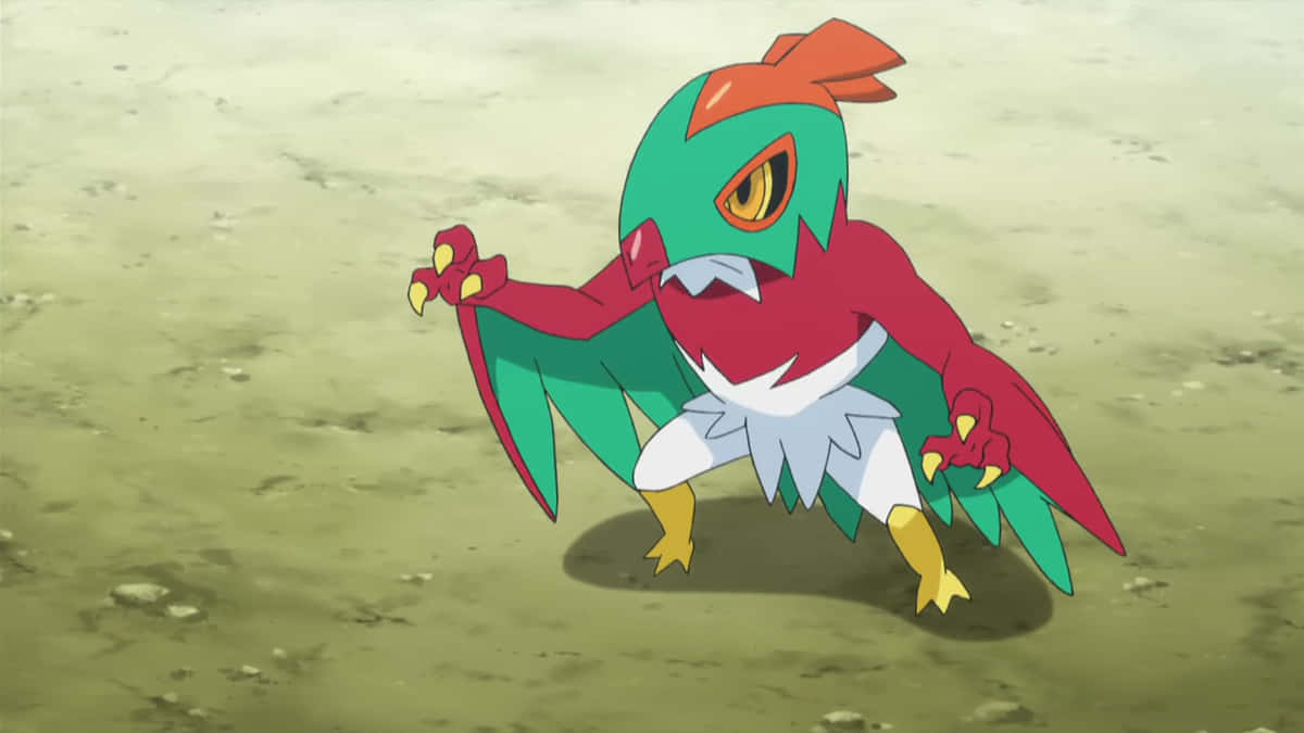 Hawlucha 動畫地面姿態 壁紙 — 一隻充滿活力的動漫風格鳥類寶可夢，擁有綠色、紅色和白色的羽毛，警覺地站在沙地上。