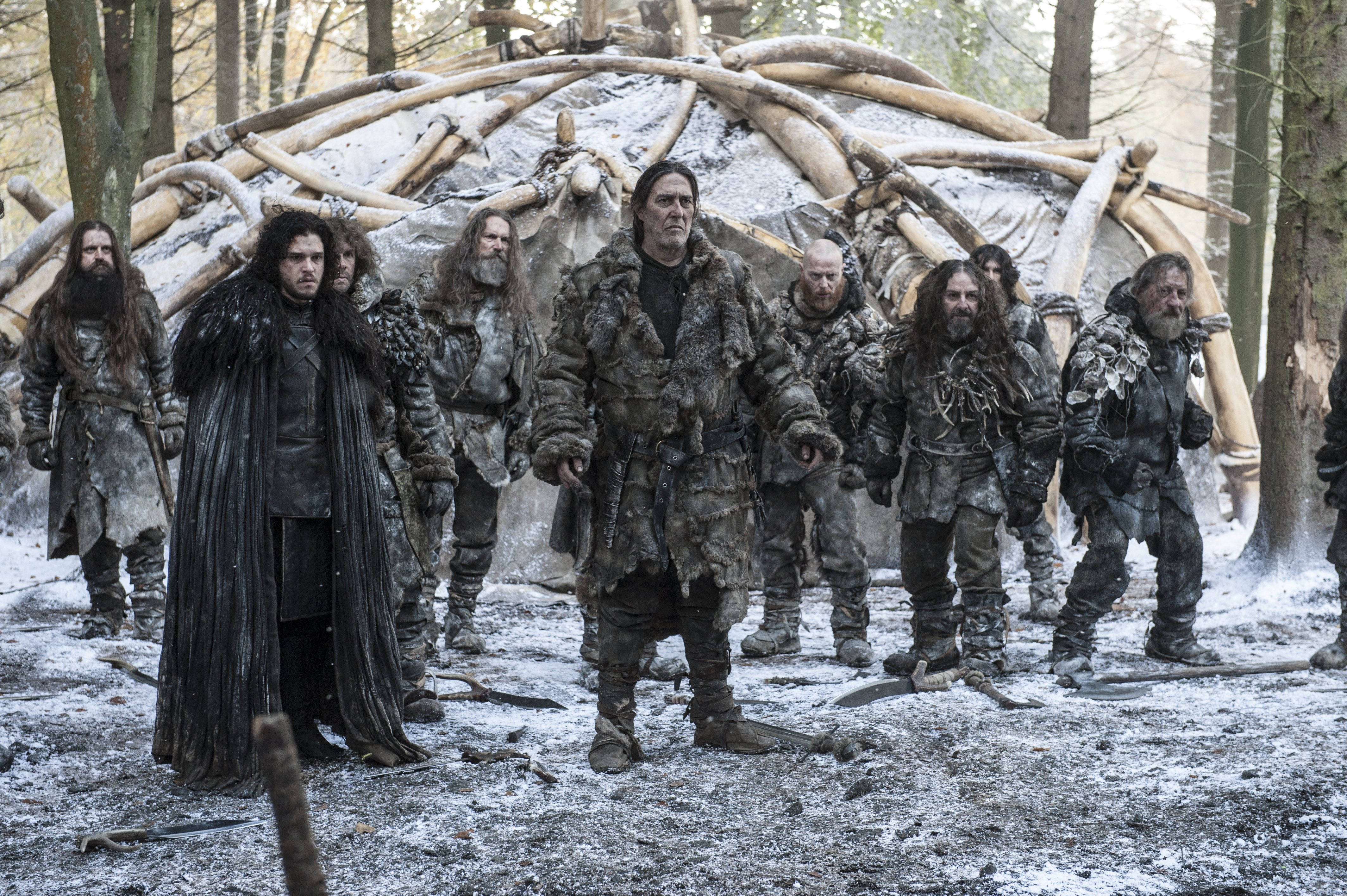 HBO《冰與火之歌》第四季：基蘭·欣德斯飾演曼斯·雷德 壁紙 — 一群粗獷、沾滿雪花的戰士，身穿毛皮和皮革，站在冬日森林中一個由骨頭和獸皮搭建的庇護所前。